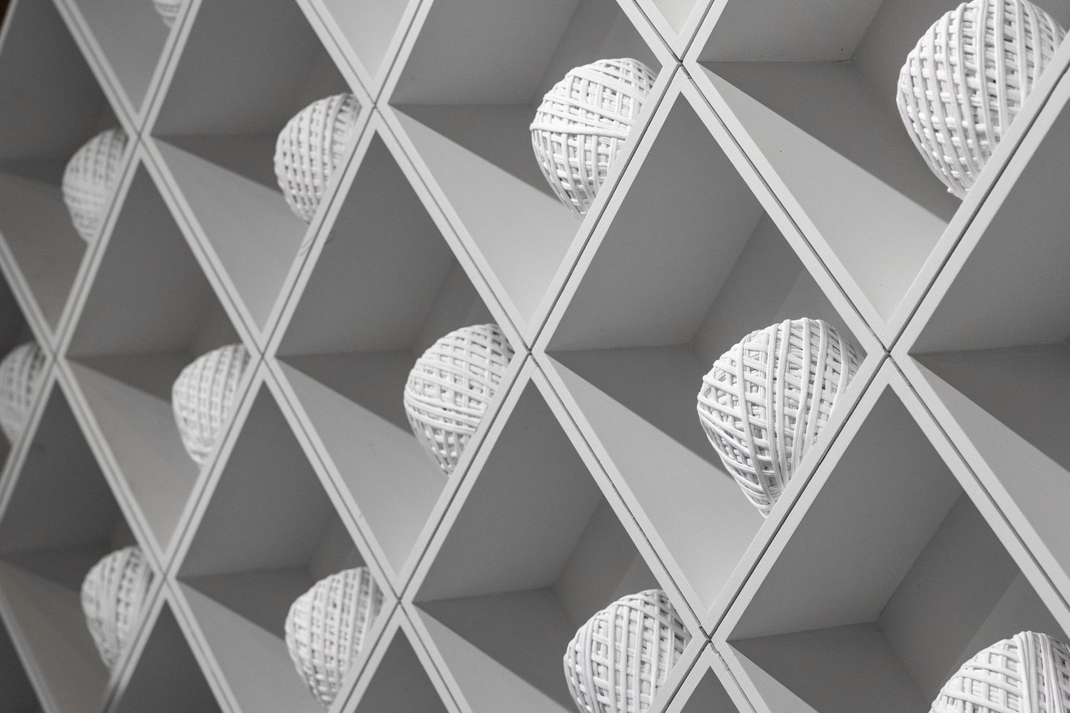 Close-up of white geometric diamond-grid shelving with decorative woven sphere ornaments in each angular compartment.
