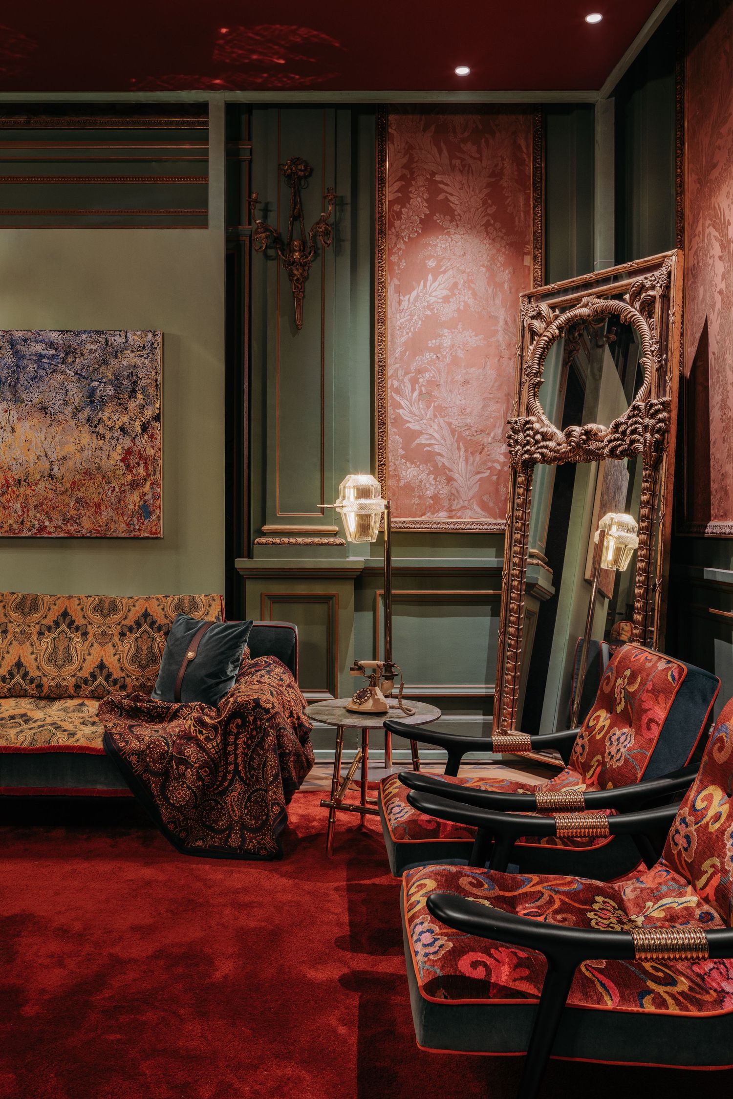 Opulent red and green vintage room with ornate mirror, patterned chairs, and rich velvet furnishings.