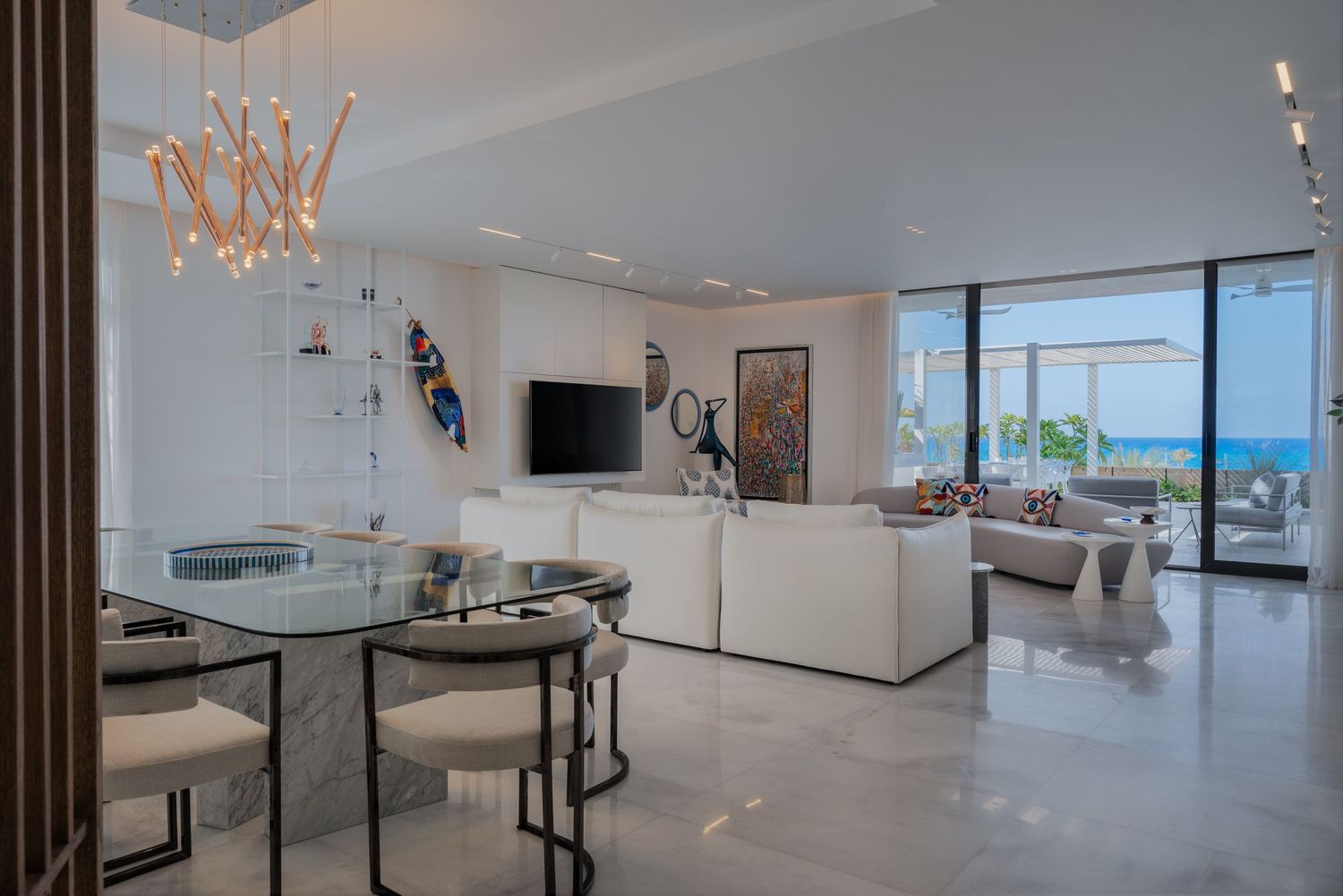Spacious modern living room with white sofa, glass dining table, and floor-to-ceiling ocean view windows.