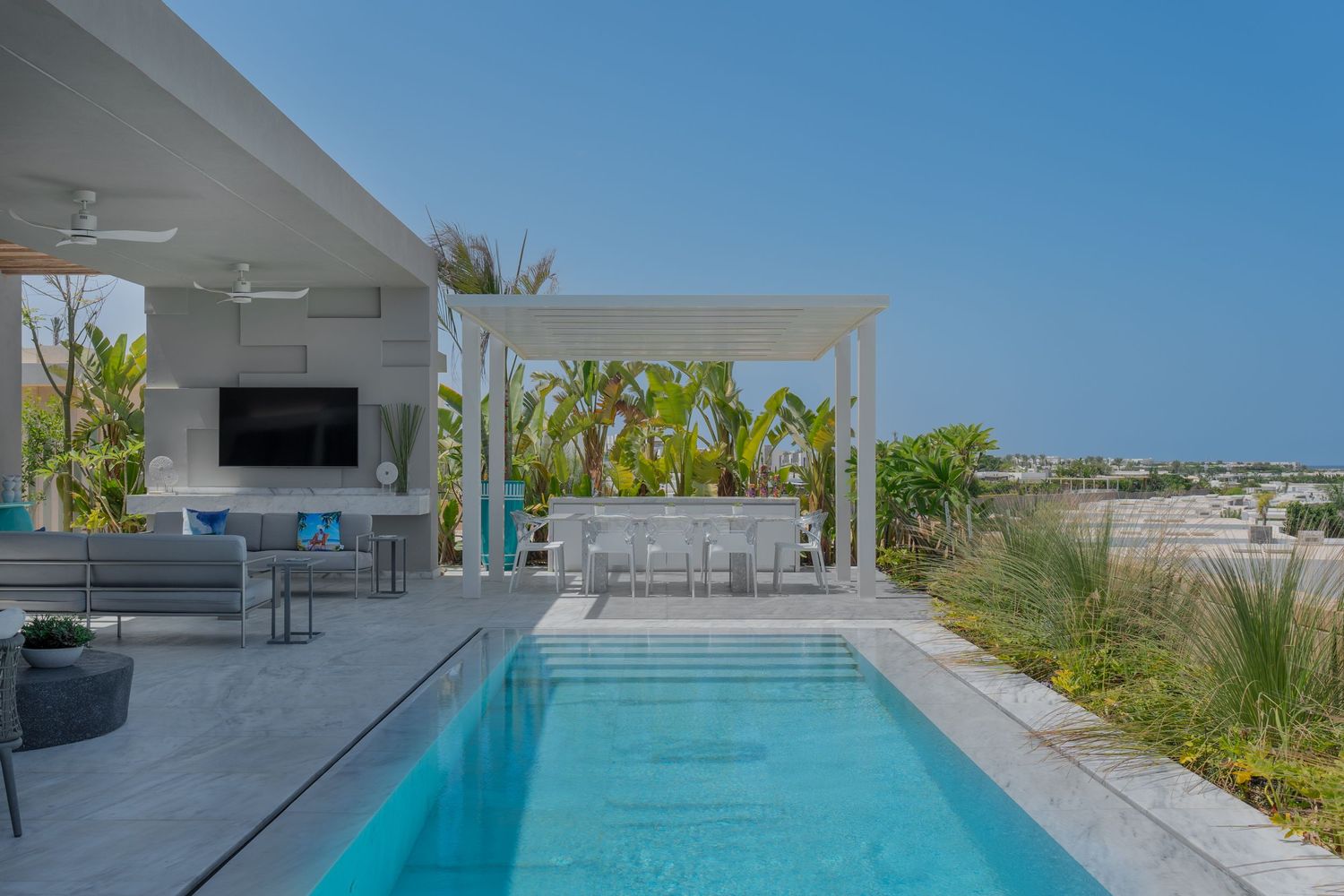 Luxury villa outdoor pool area with pergola, bar seating, ceiling fan, and tropical garden views.