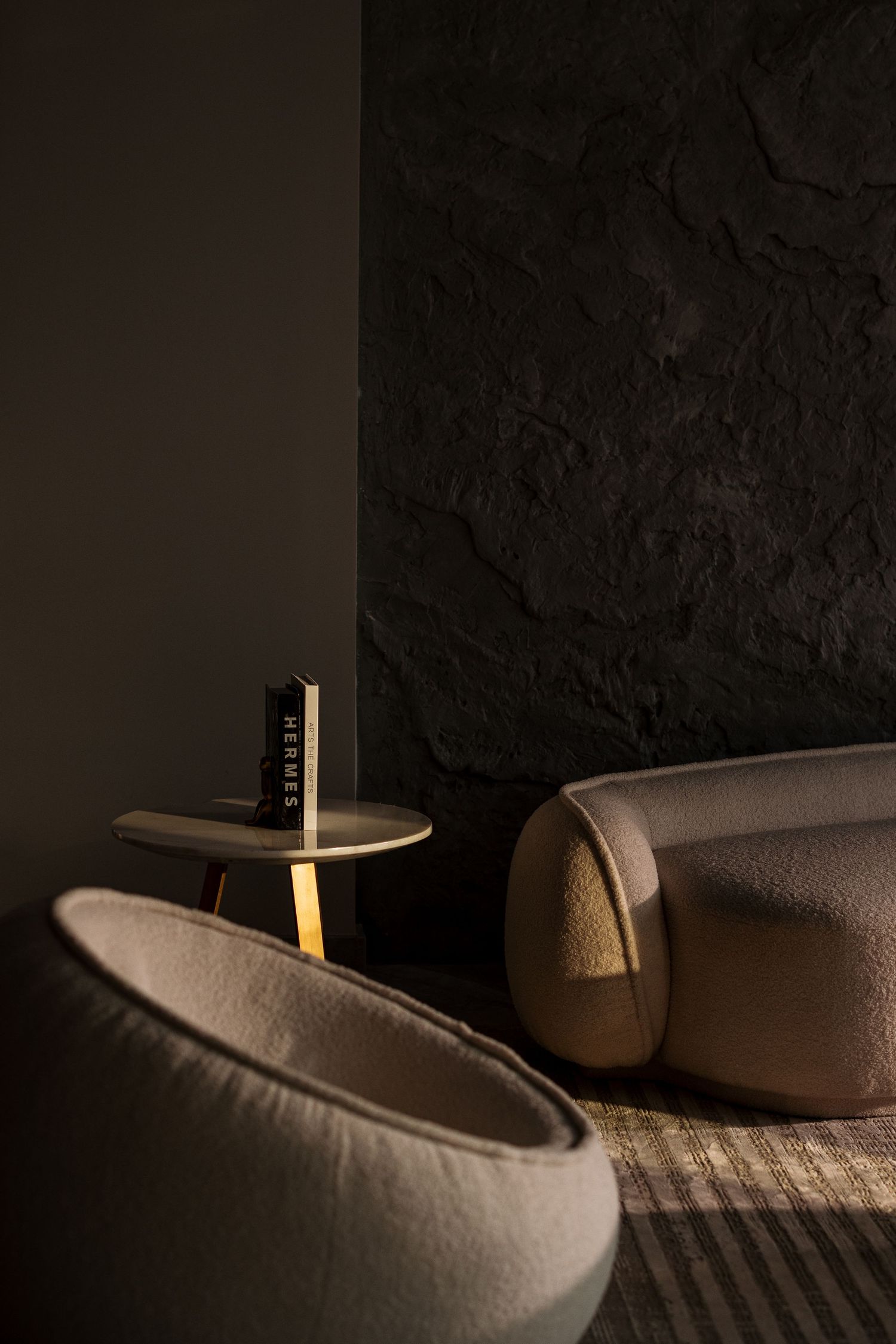 Dark moody living room corner with curved beige sofa, round side table, and glowing lamp against textured black wall.