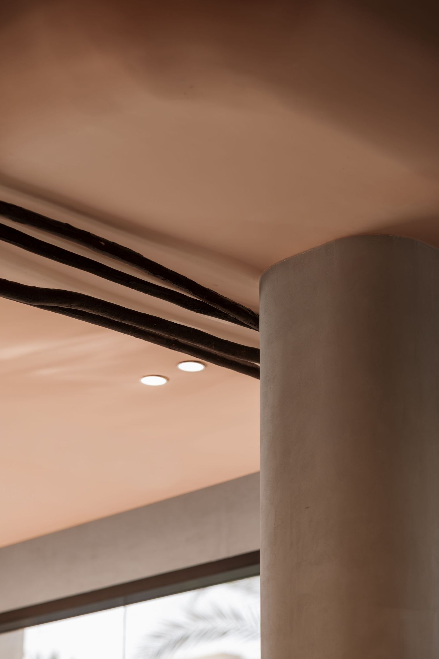 Warm terracotta ceiling detail with recessed lights, dark linear accents, and a smooth concrete column in modern interior.