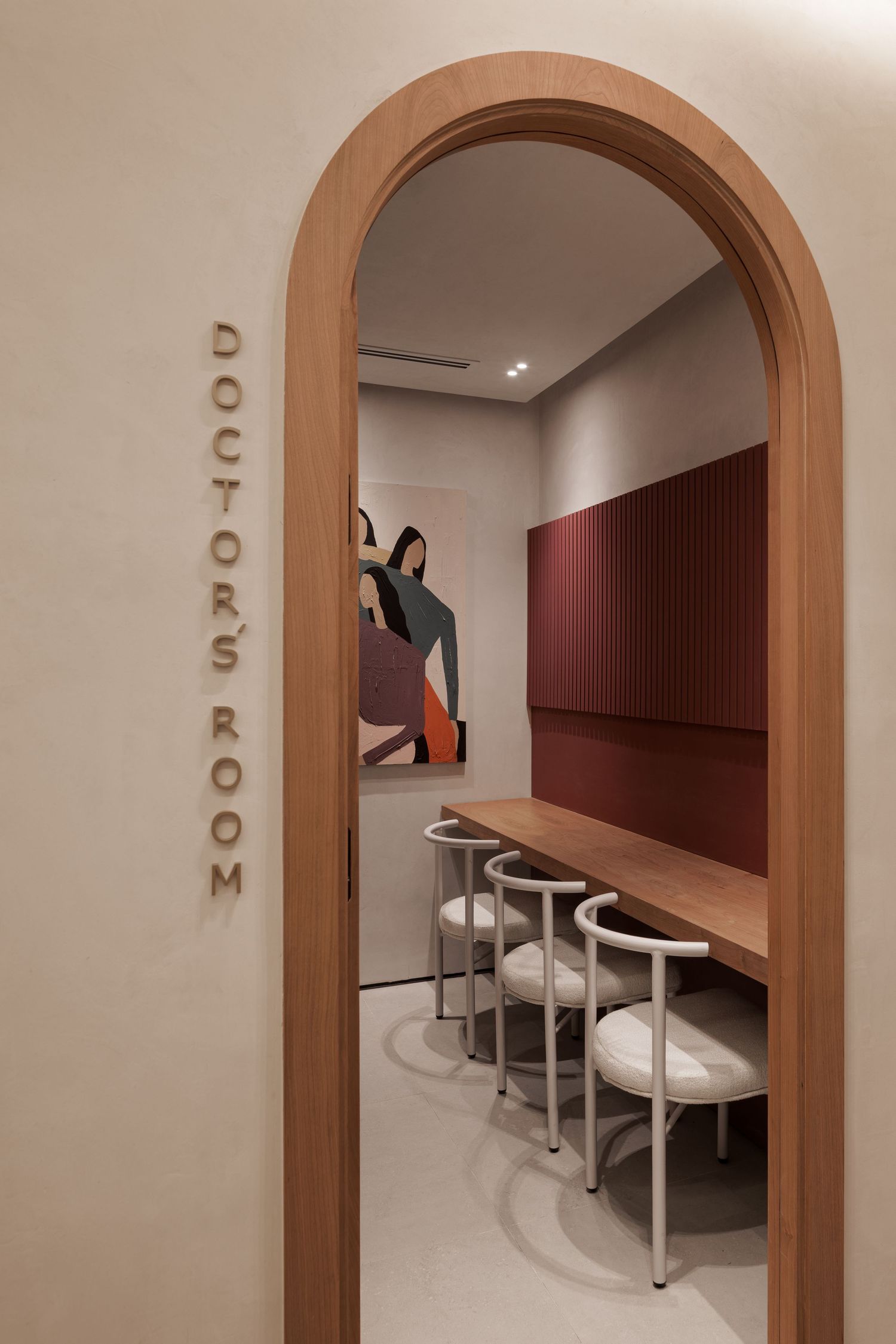 Warm arched wooden doorway leads to a cozy Doctor's Room with burgundy panels, white chairs, and abstract wall art.
