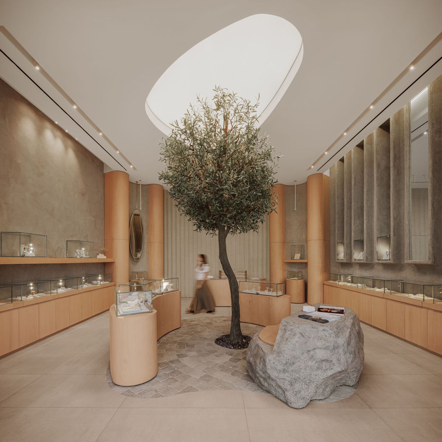 Elegant jewelry boutique interior featuring large olive tree centerpiece, rock display, and illuminated glass showcases.