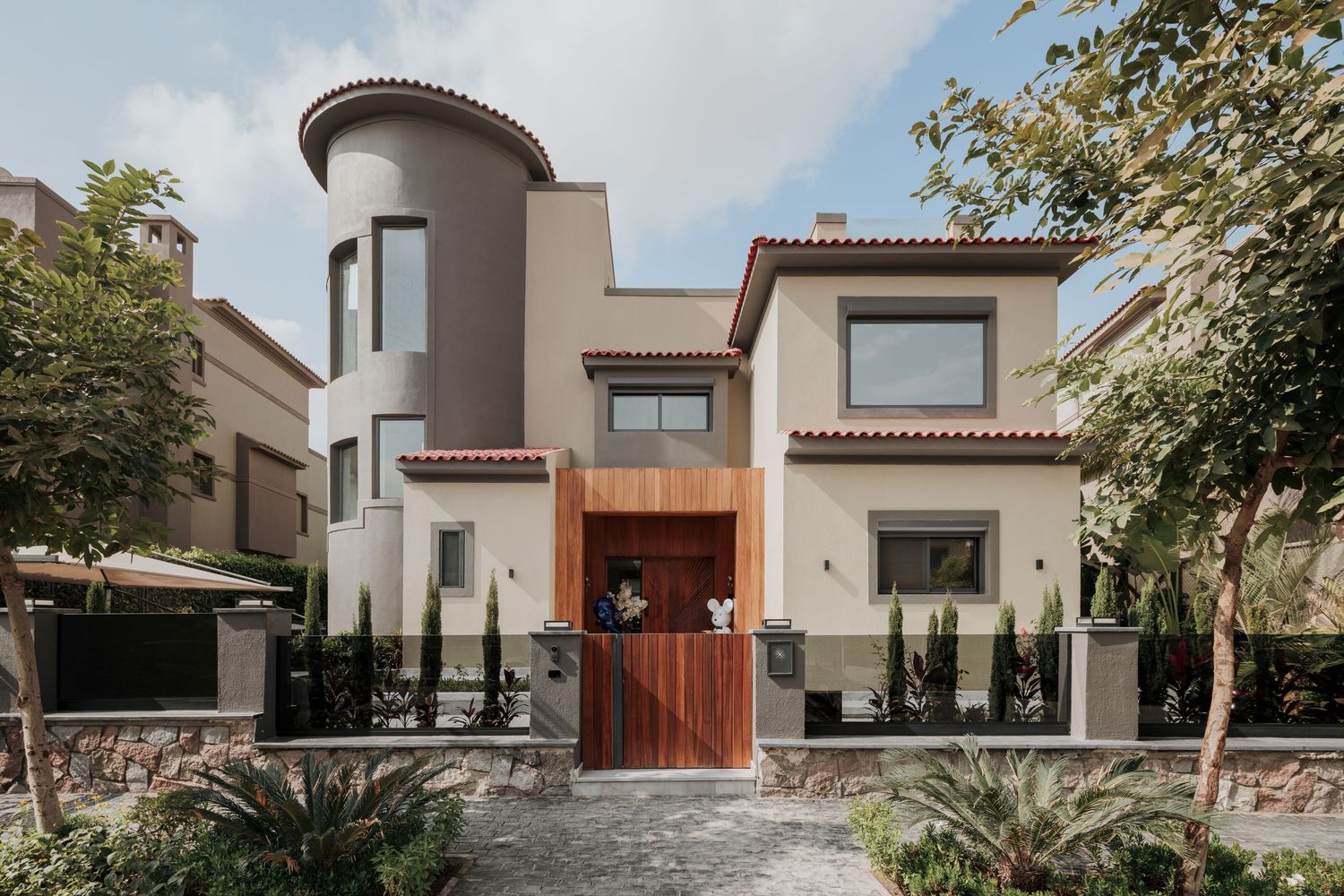 Mediterranean-style two-story villa exterior with stucco facade, wooden gate, and lush landscaped front garden.