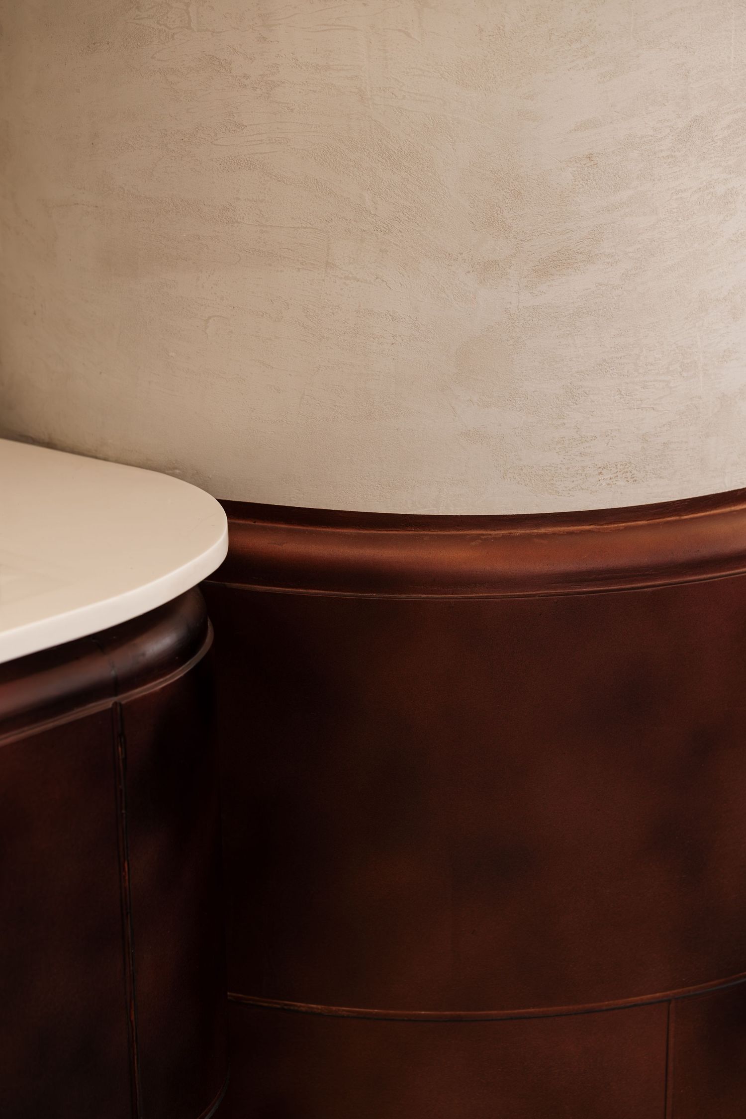 Detail of a curved dark brown leather wall panel with a white marble countertop against a textured beige wall.