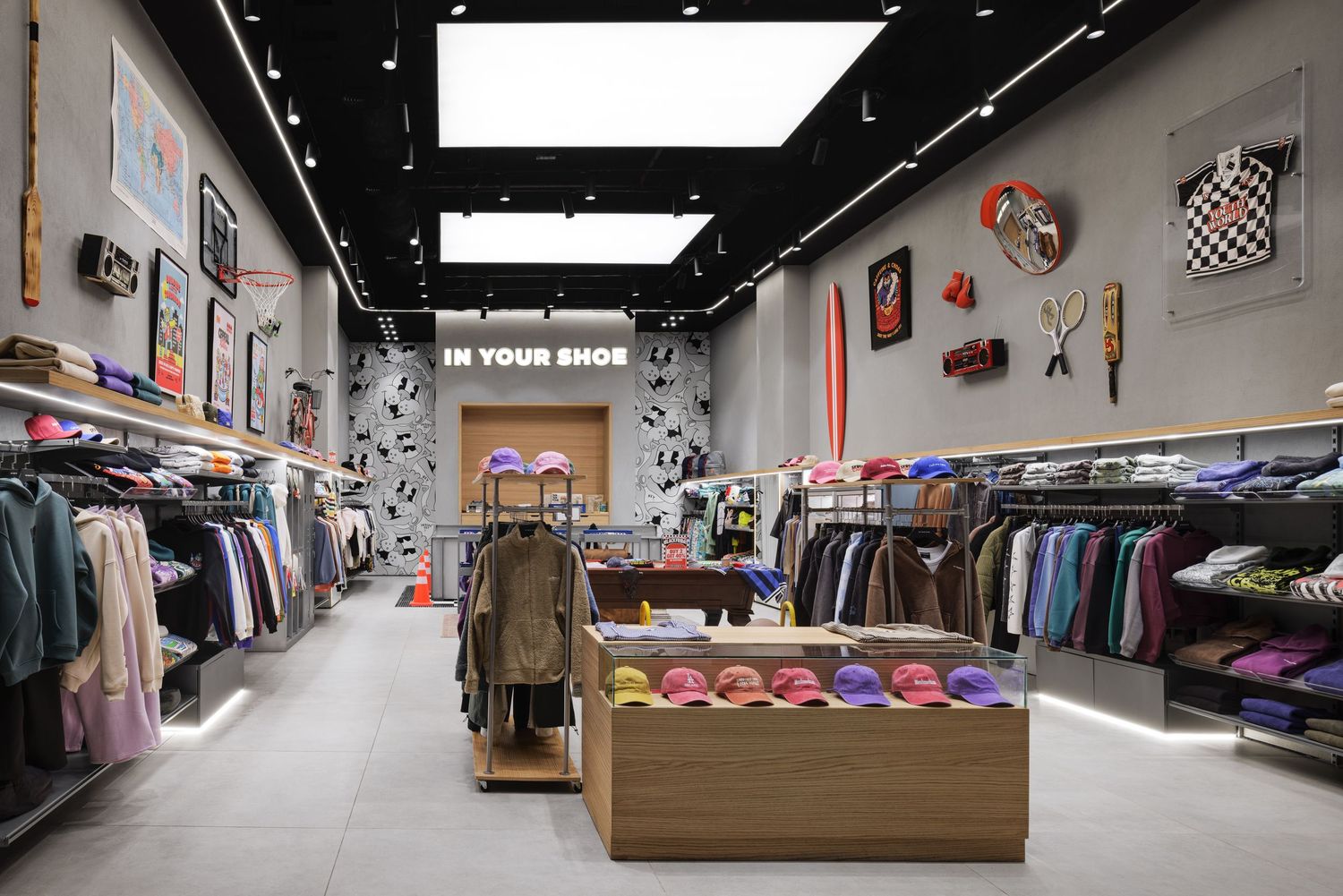 Colorful streetwear clothing store interior with wall art, hats display, and apparel racks under skylight.