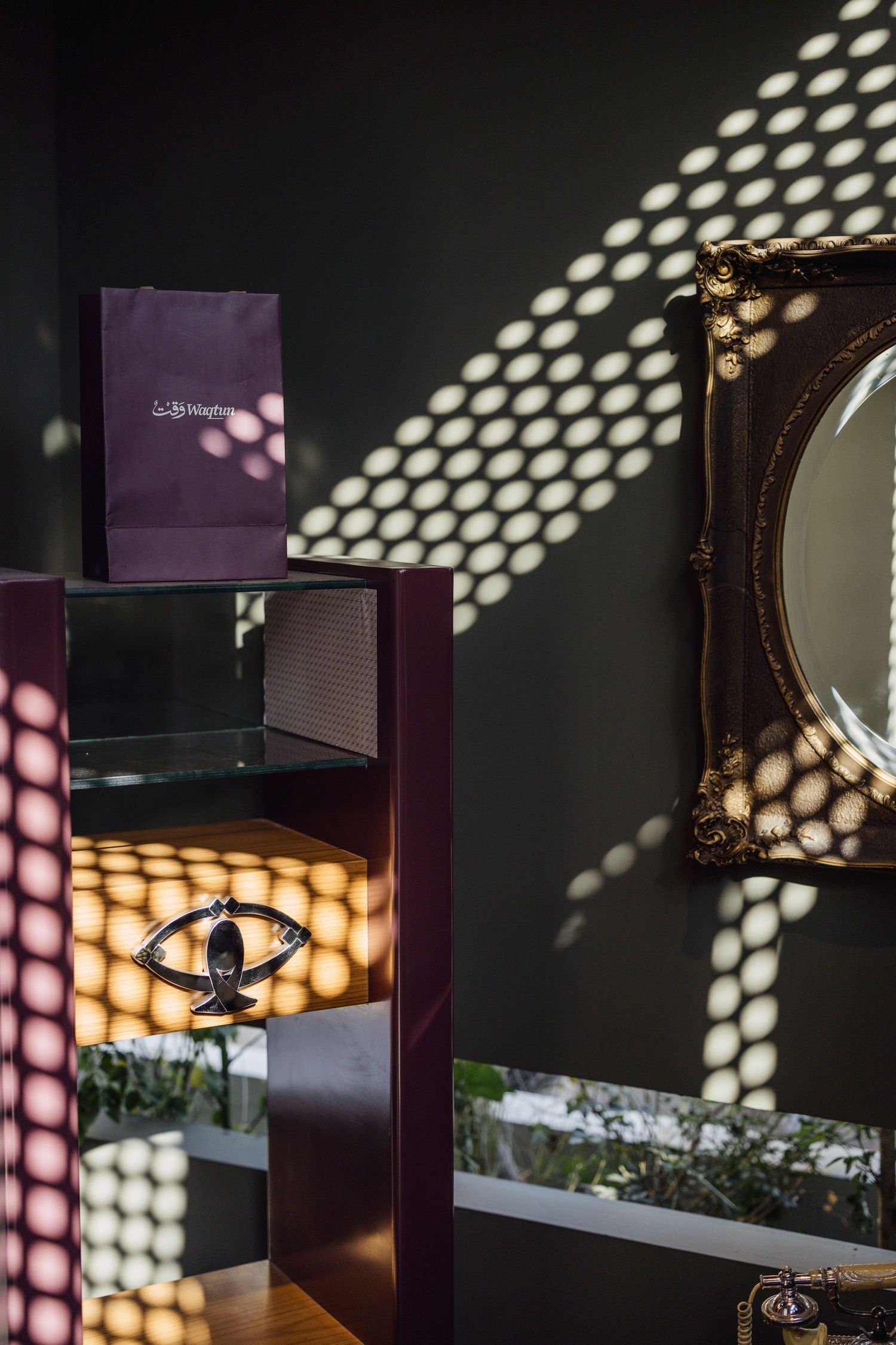 Decorative shelf with purple gift bag, ornate mirror, and dappled light patterns on dark wall.