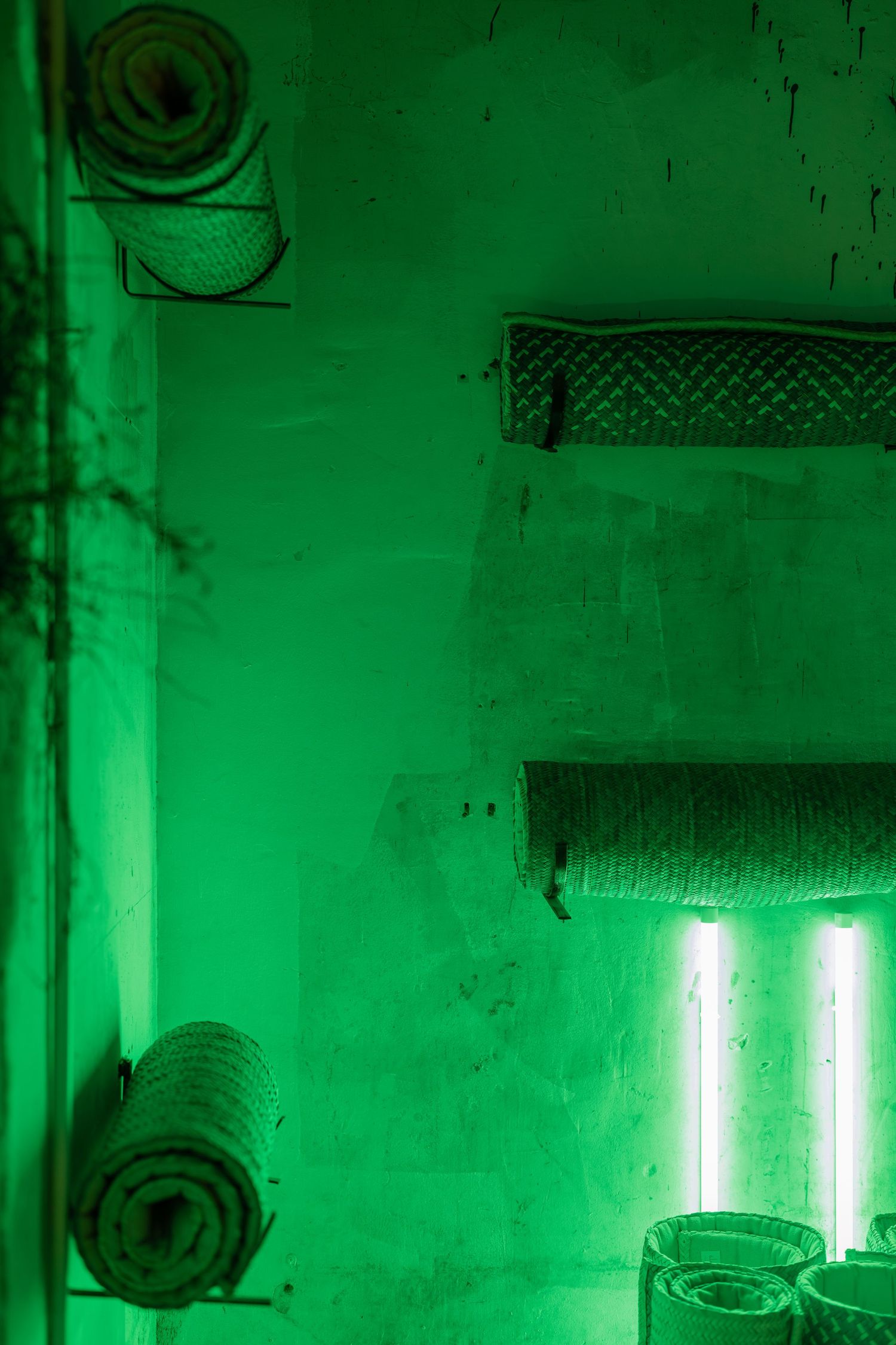 Room bathed in green neon light with rolled towels on wall-mounted racks and a glowing tube light.