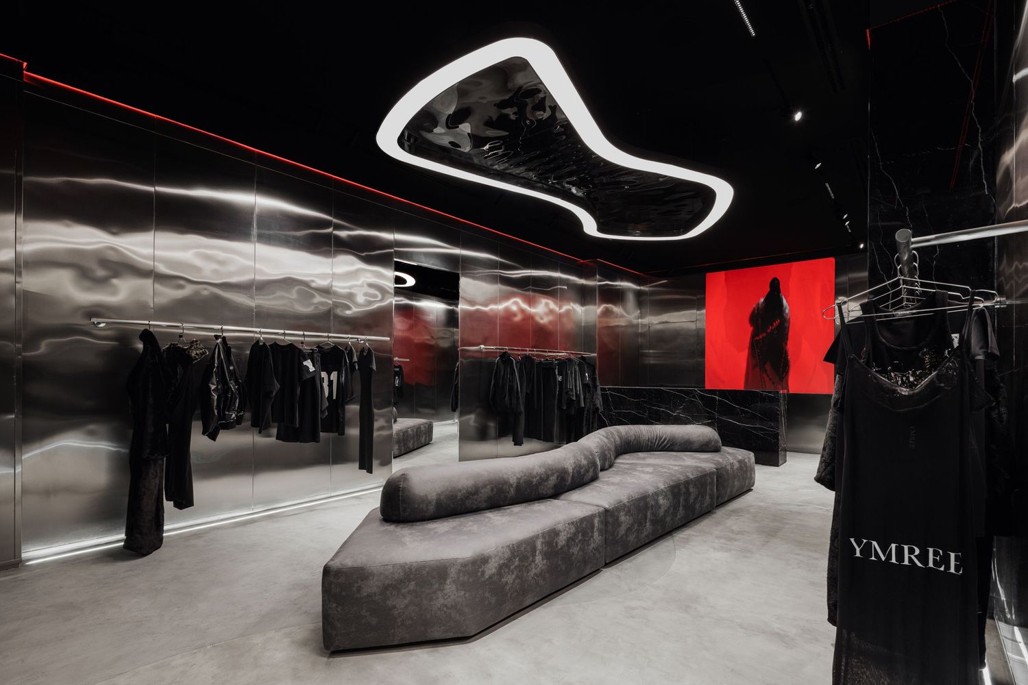 YMREL fashion boutique interior with black metallic walls, curved white neon ceiling light, and dark clothing displays.
