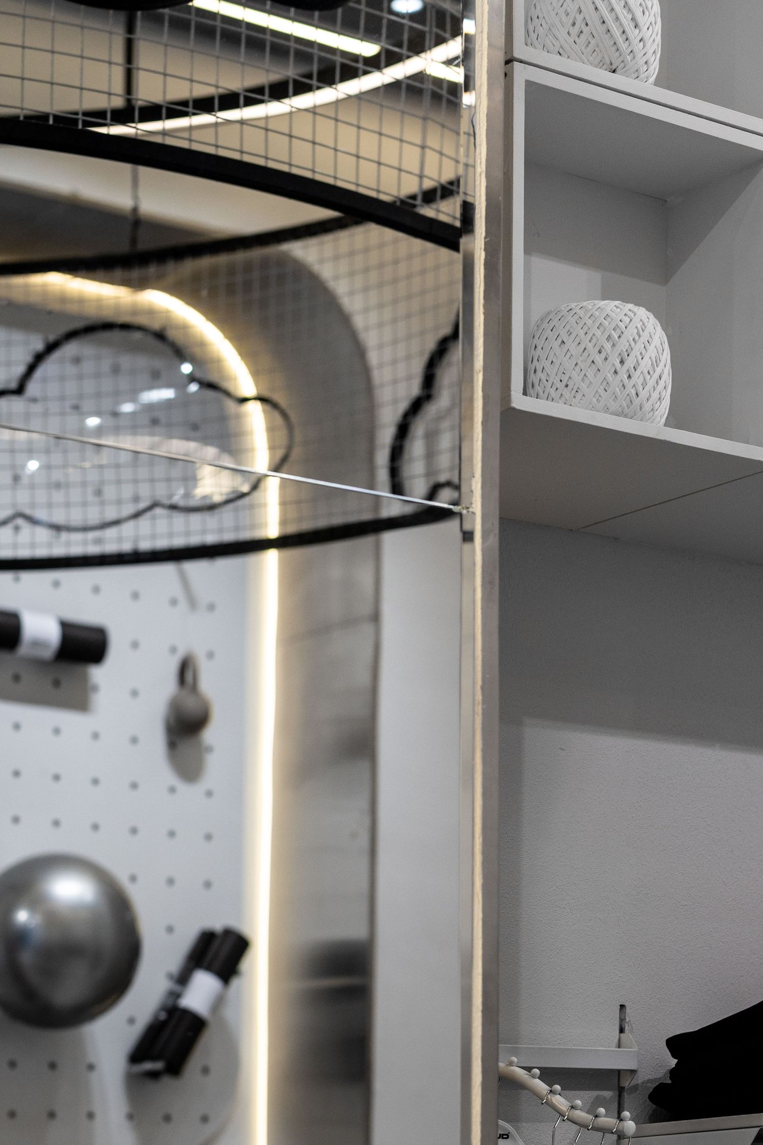 Modern retail store interior with pegboard wall display, LED lighting, shelving, and decorative woven spheres.