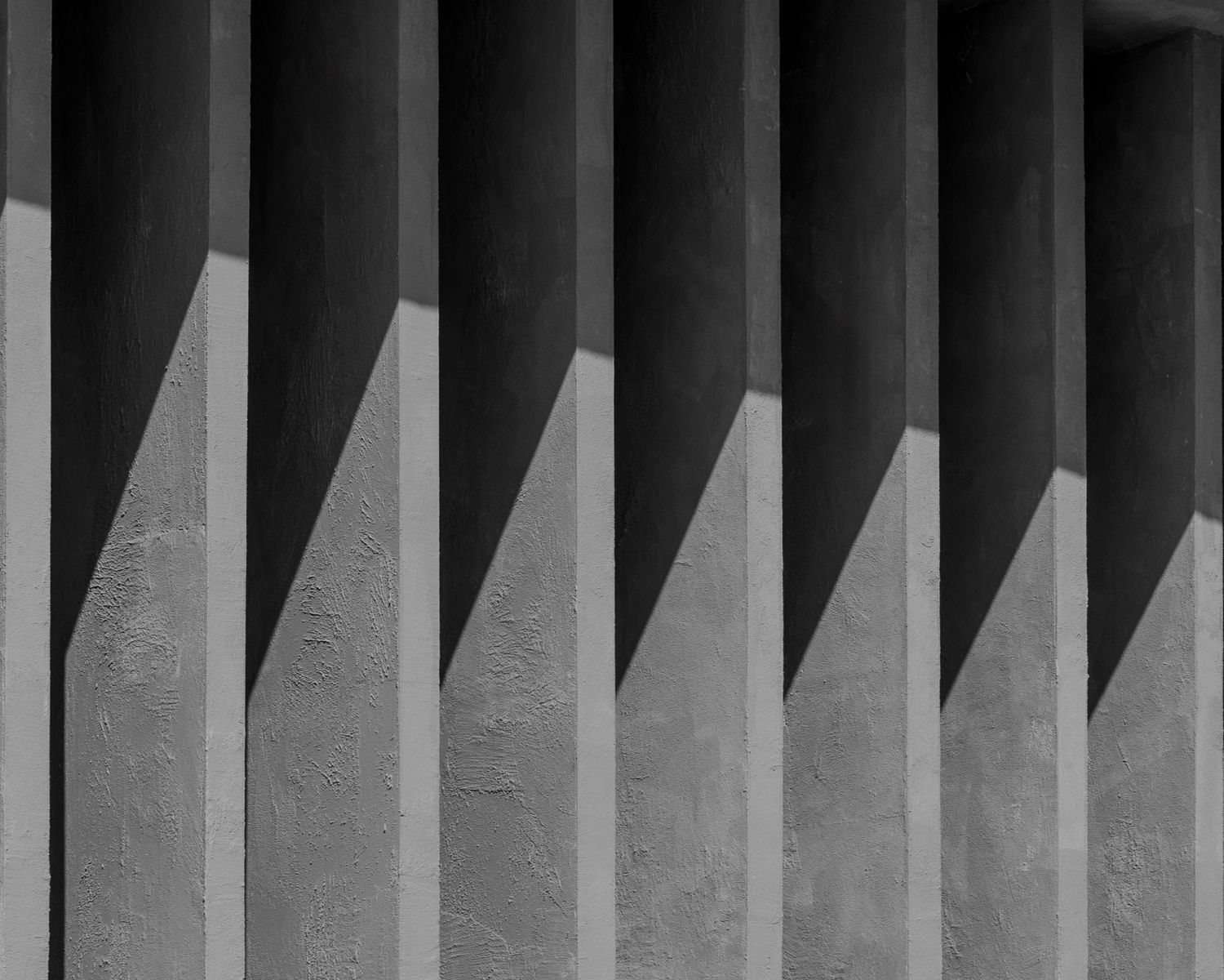 Black and white abstract architectural photo of repeating concrete columns with shadows.