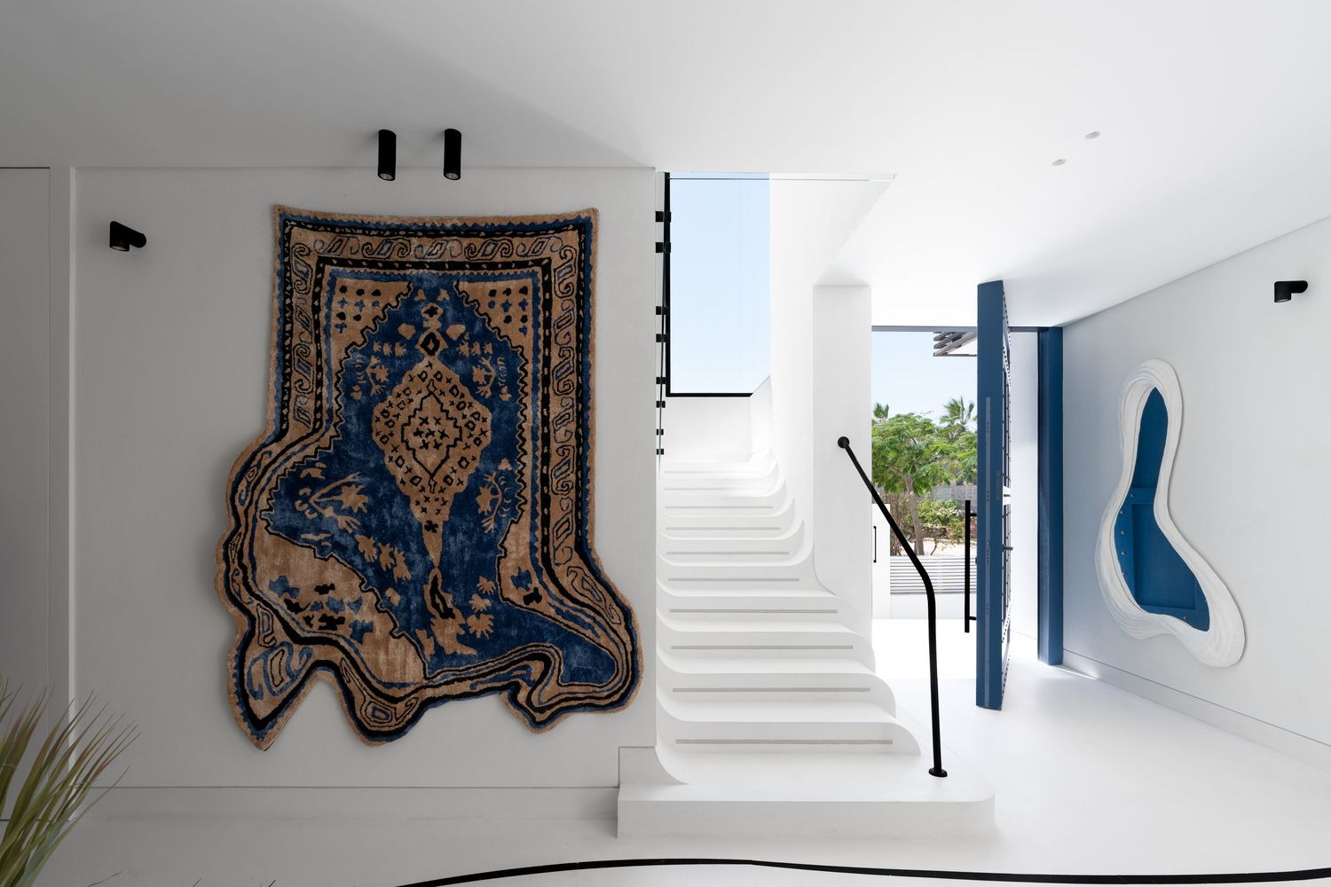 Elegant white staircase with a decorative blue Persian rug wall hanging and abstract blue art piece in a modern luxury home.