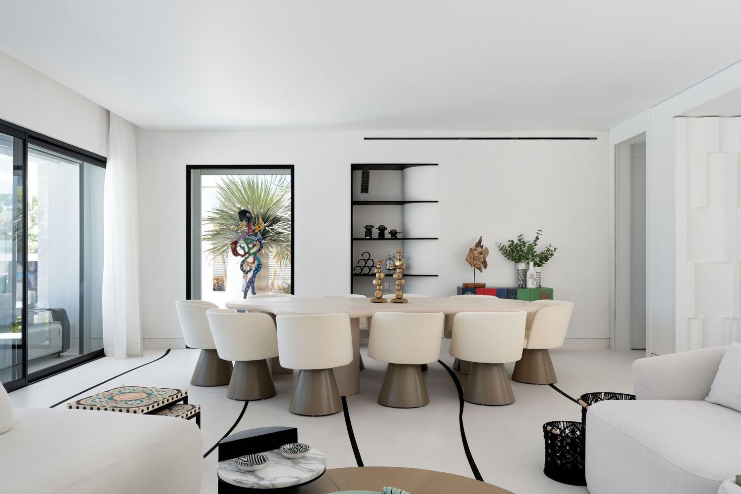 Elegant white dining room with cream barrel chairs, wooden table, and floor-to-ceiling garden window.