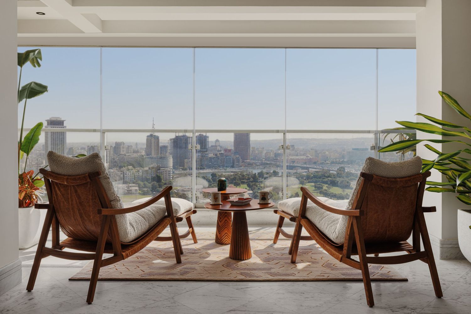 Modern high-rise living room with floor-to-ceiling windows, mid-century wooden chairs, and panoramic city skyline views.