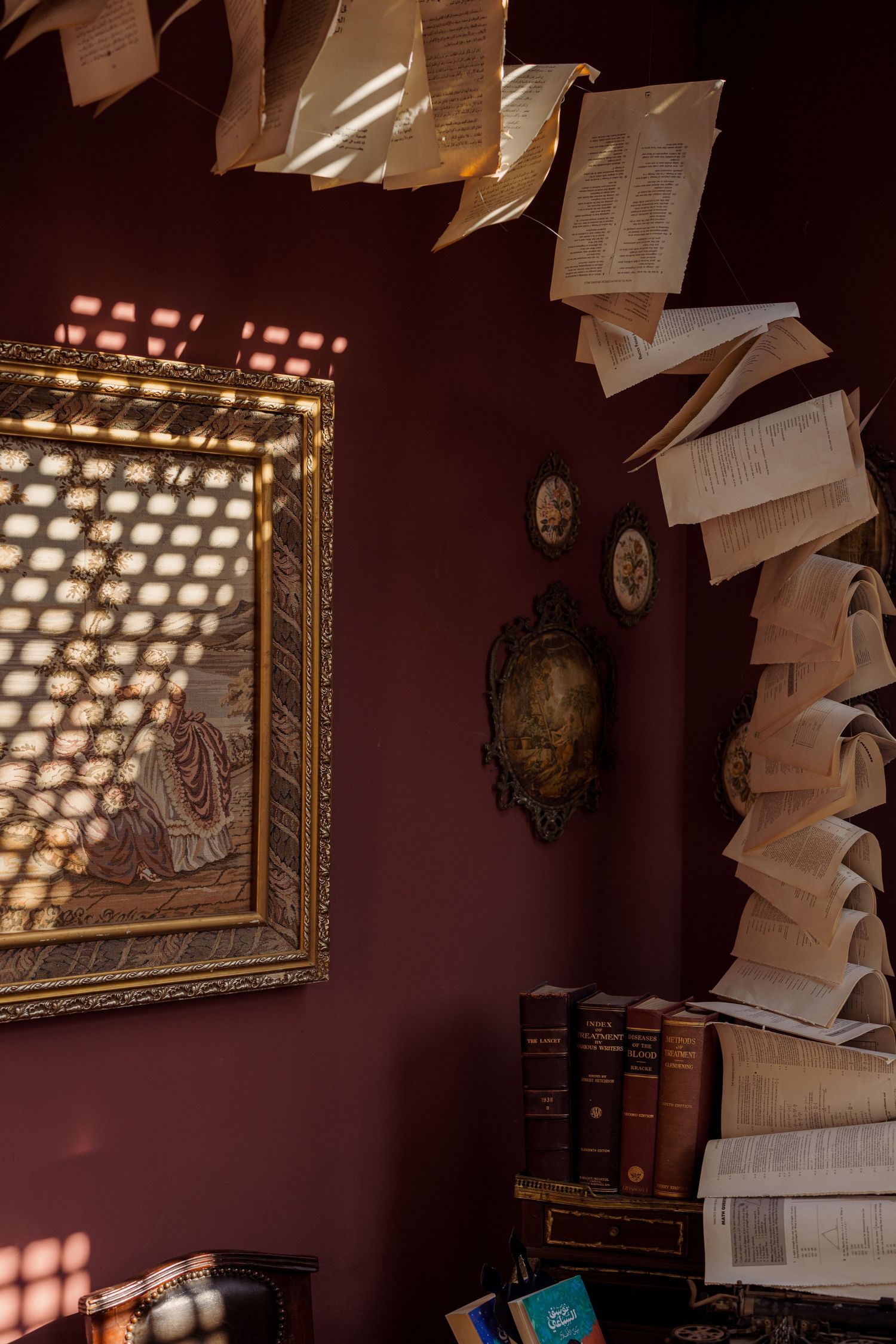 Pages of books floating against a dark red wall with vintage frames and antique books below.