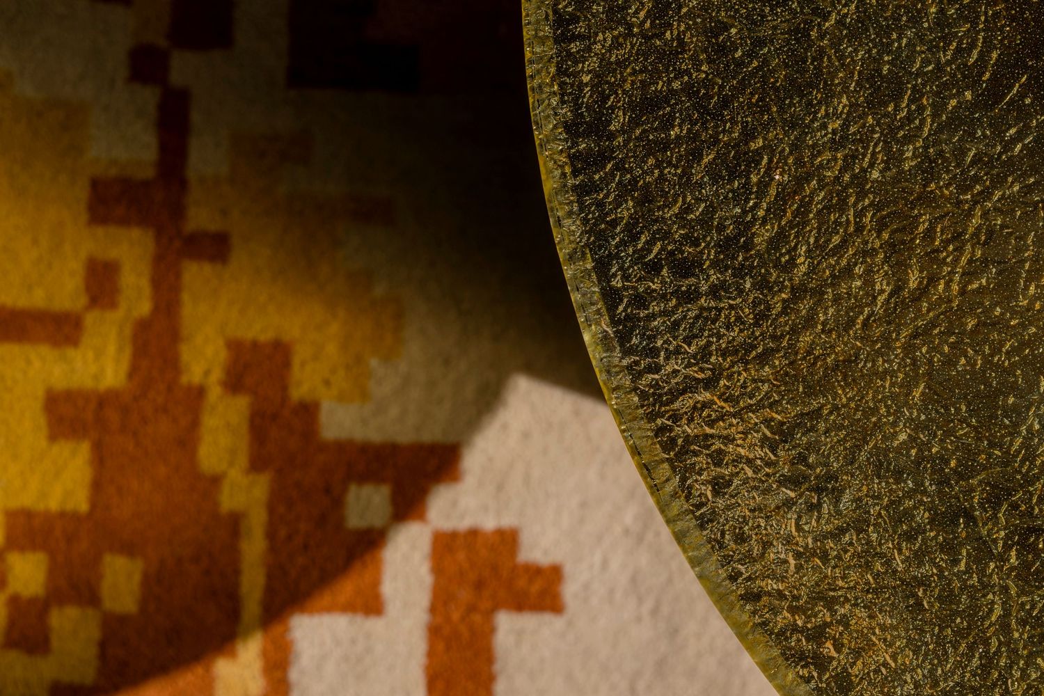 Close-up of golden textured surface beside colorful pixel-pattern fabric in warm earth tones.