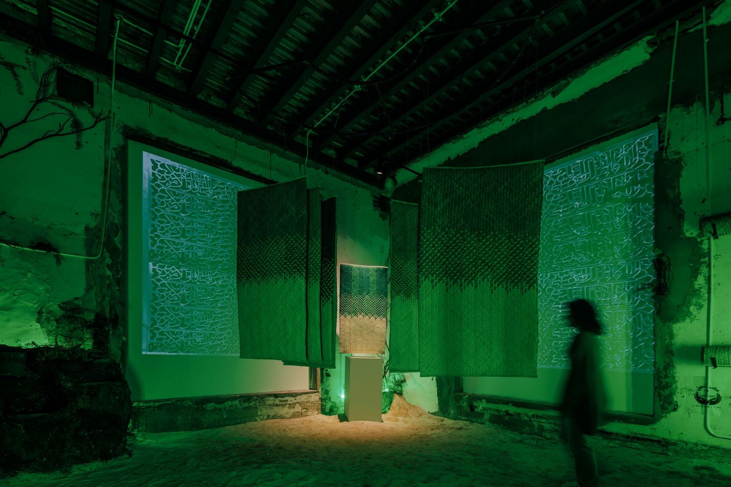 Immersive green-lit installation with woven panels and central glass structure in a historic building.