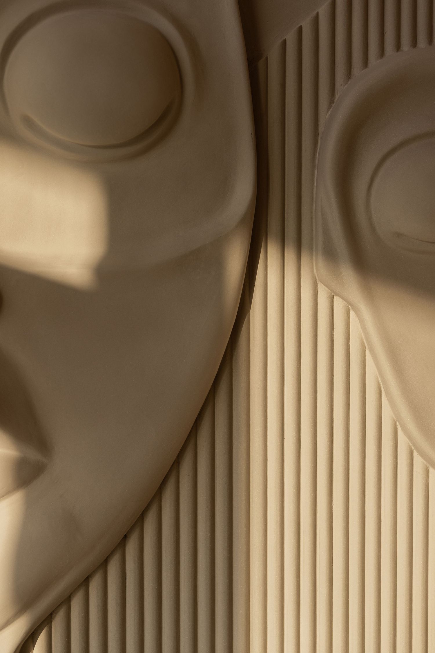 Close-up detail of beige sculptural face relief with circular eye recesses against ribbed wooden wall panel.