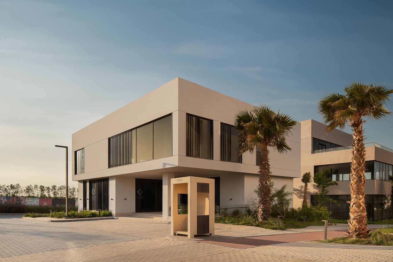 Modern two-story beige building with large windows and palm trees at golden hour in a luxury development.