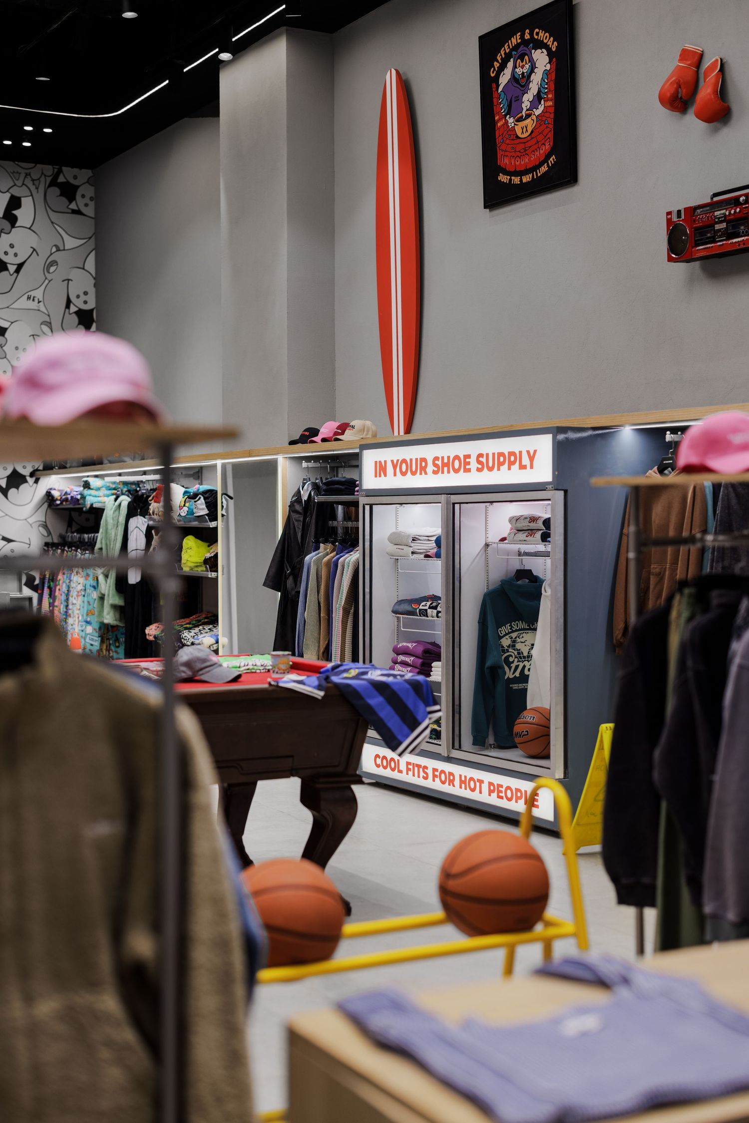 Trendy streetwear store interior with surfboard wall decor, basketballs, clothing racks, and cool urban retail displays.