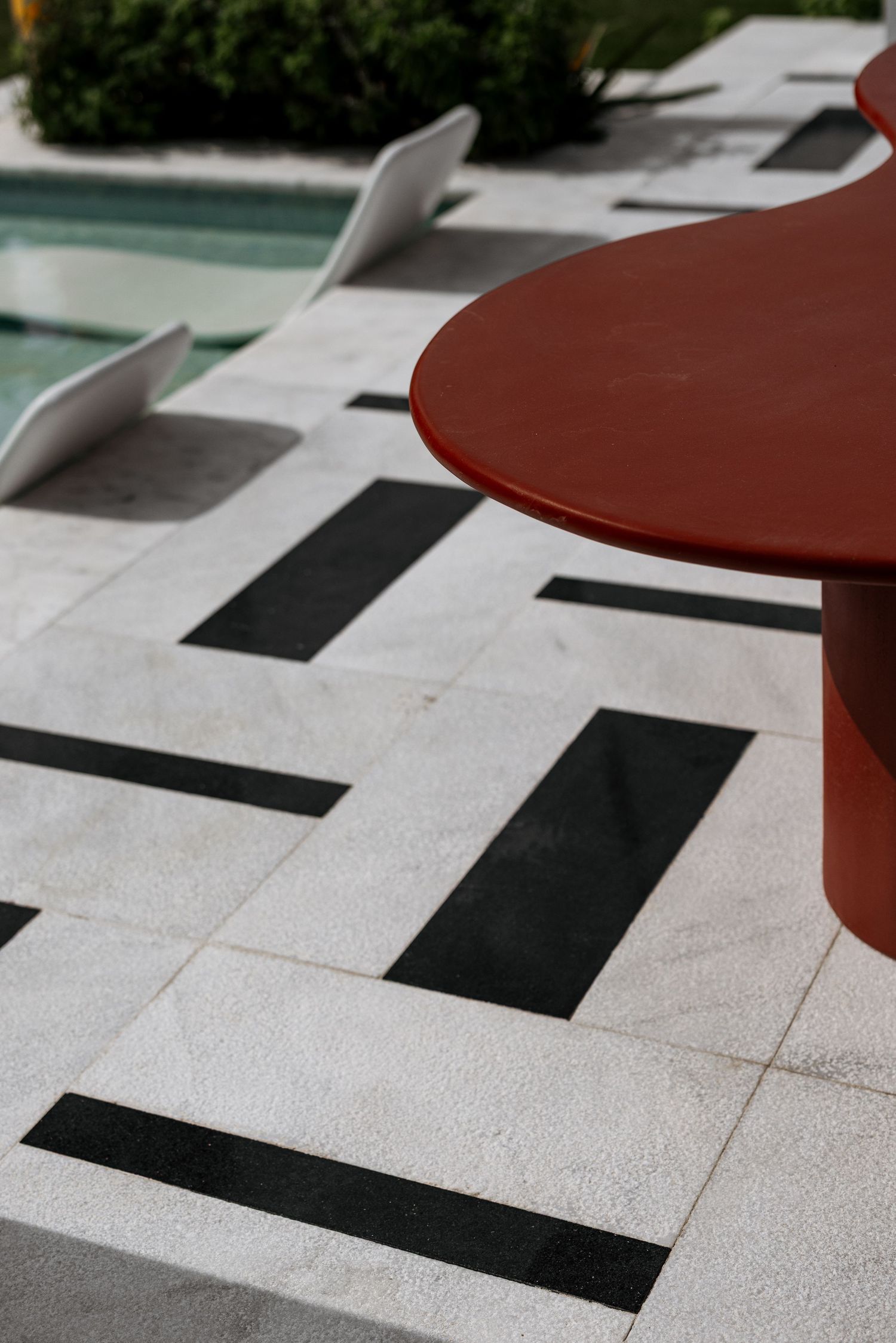 Bold black and white geometric tile pool deck with red curved table and white lounge chair detail.