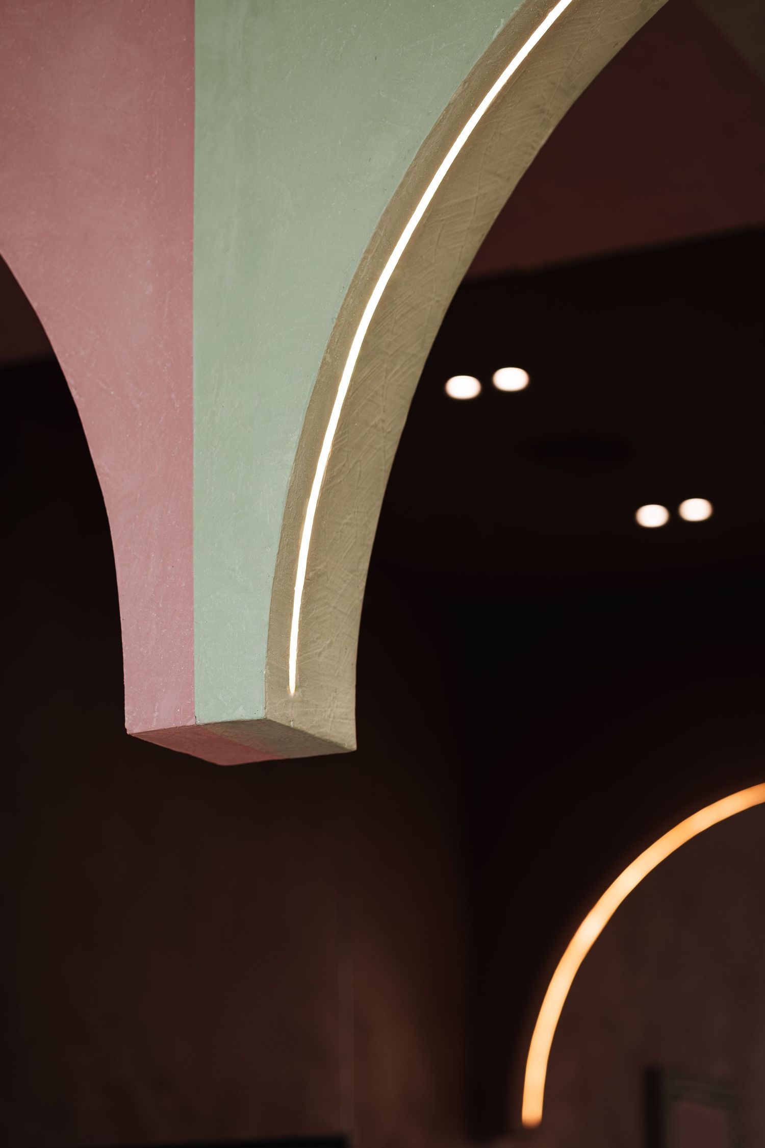 Illuminated arched doorway with sage green and pink plaster walls and recessed ceiling spotlights.