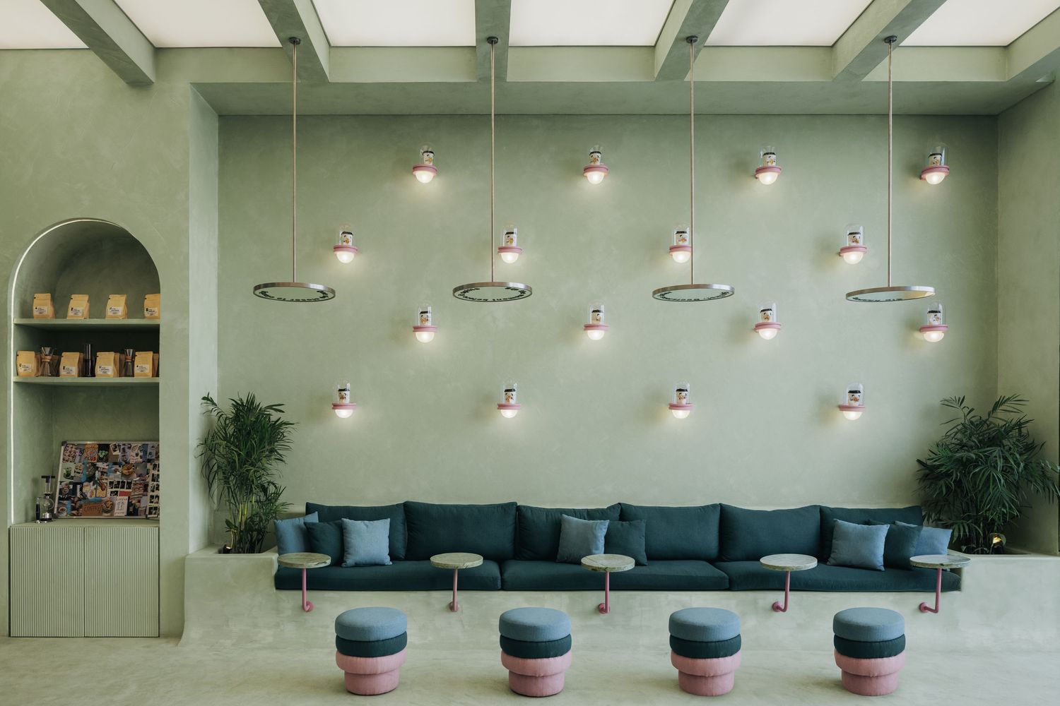 Spacious sage green lounge with teal sofas, pink ottomans, and multiple decorative pendant lights.