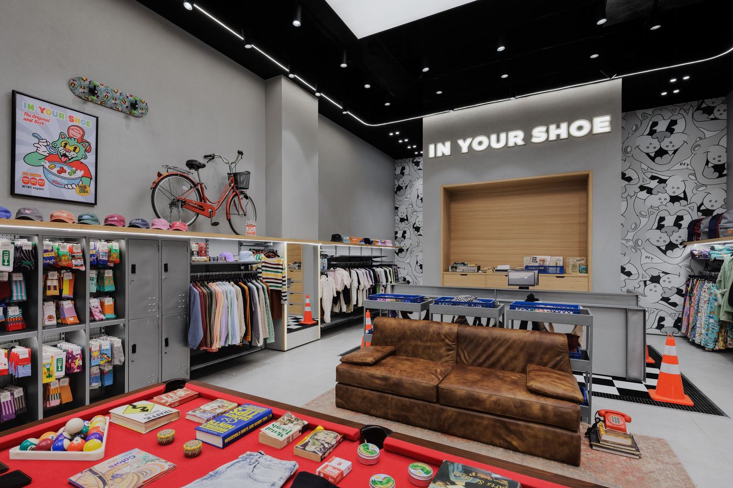 In Your Shoe retail space featuring a leather sofa, red bicycle, colorful merchandise displays, clothing racks, and graphic wall art.