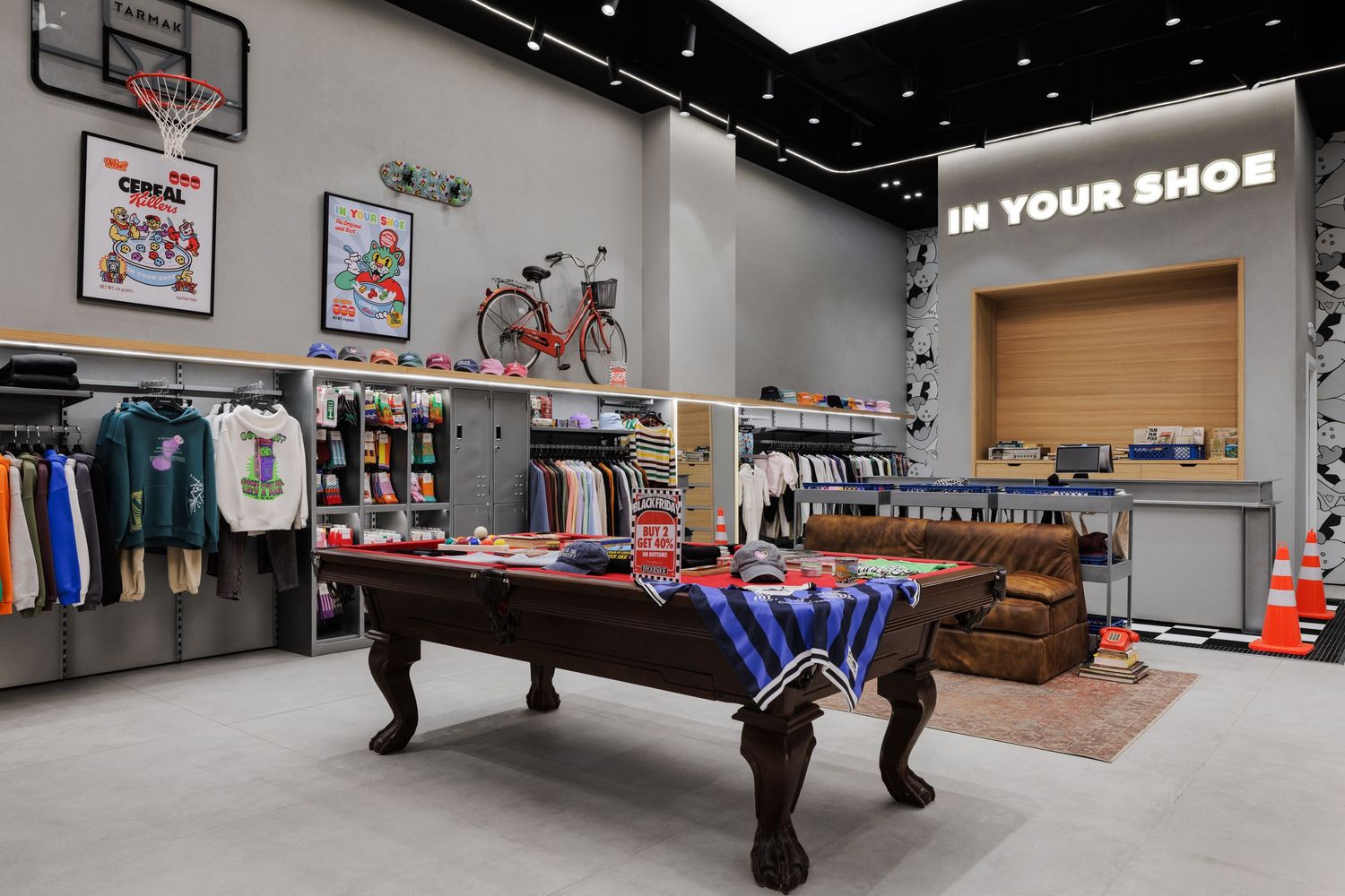 In Your Shoe store interior showcasing a pool table, hanging apparel, wall art, and a red bicycle as a decorative element.