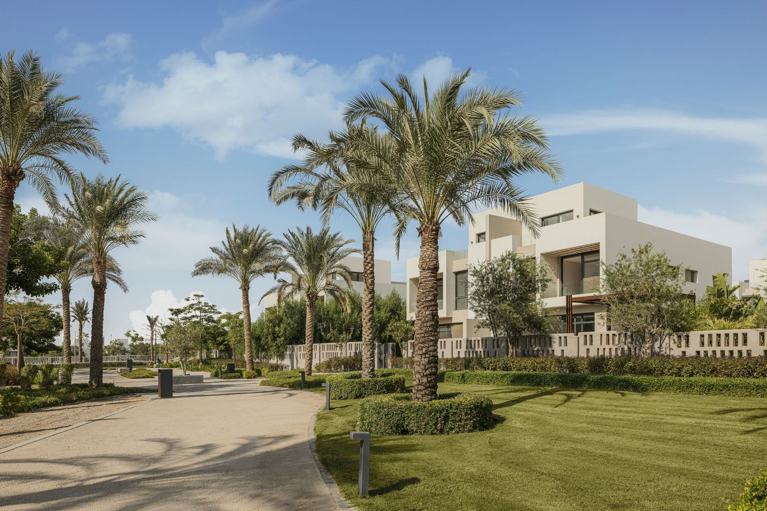 Luxury modern villas surrounded by tall palm trees and lush green lawns under a clear blue sky.