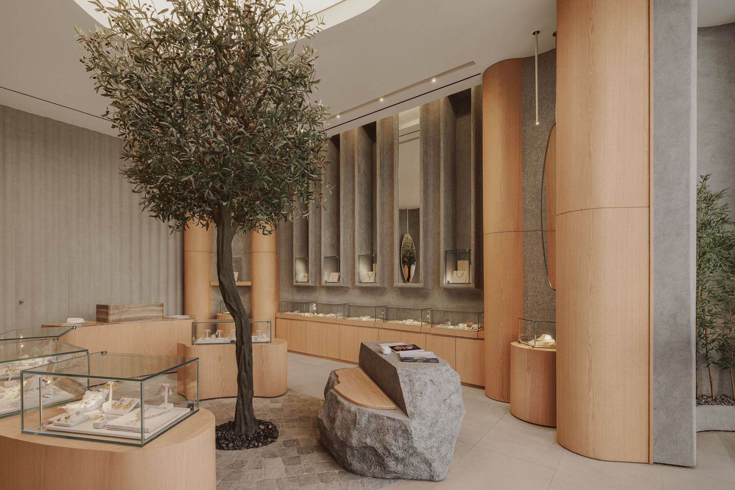 Sophisticated jewelry store with large olive tree centerpiece, natural stone bench, and curved display cabinets.