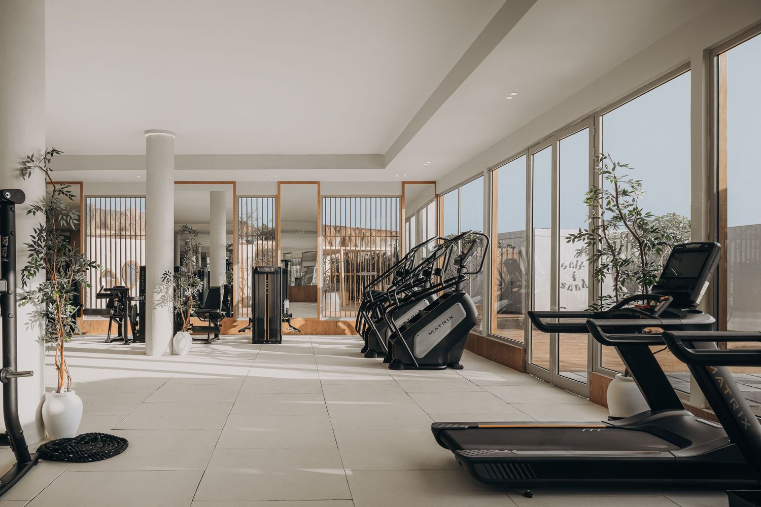 Bright modern gym interior with treadmills, large windows, natural light, and tropical views in a luxury fitness facility.