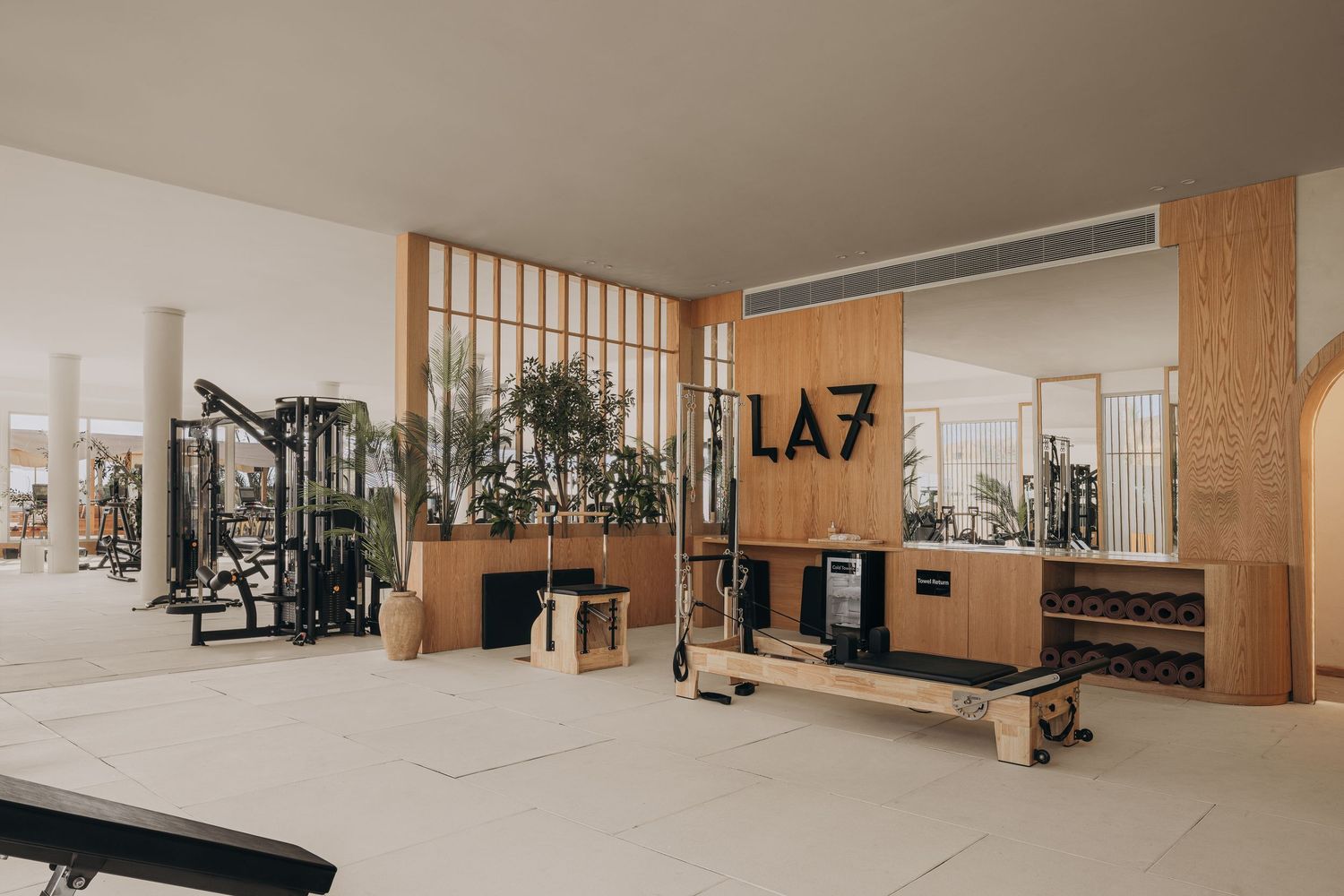 Spacious LA7 gym with pilates equipment, wooden partitions, gym machines, and natural light.