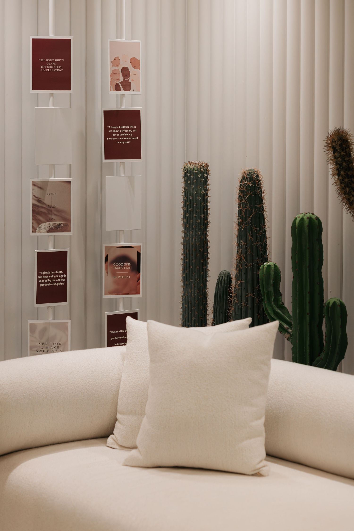Cozy cream sofa with white cushions beside tall green cacti and inspirational card display on white fluted wall panels.
