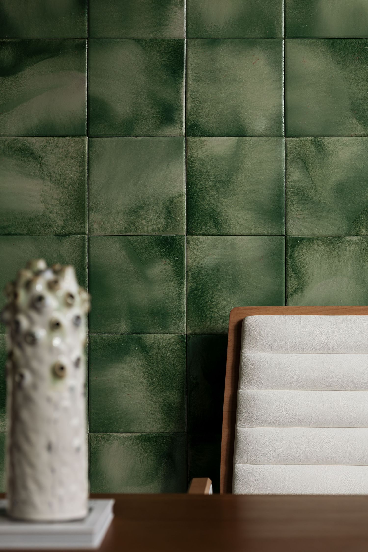 Glossy green square ceramic wall tiles with a wooden desk, white folders, and textured ceramic vase.