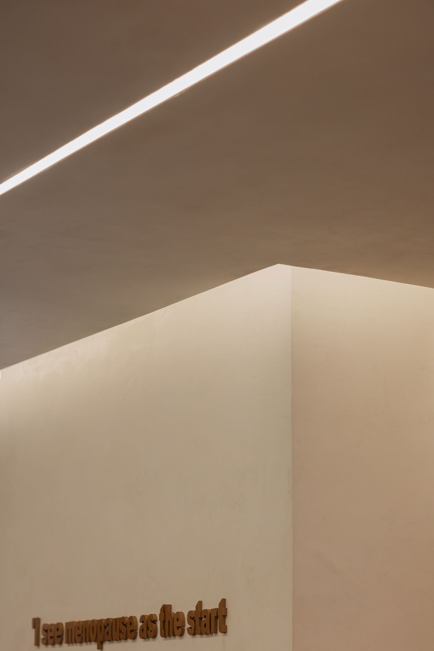 Minimalist beige interior corner with linear ceiling light and gold 3D motivational wall lettering.