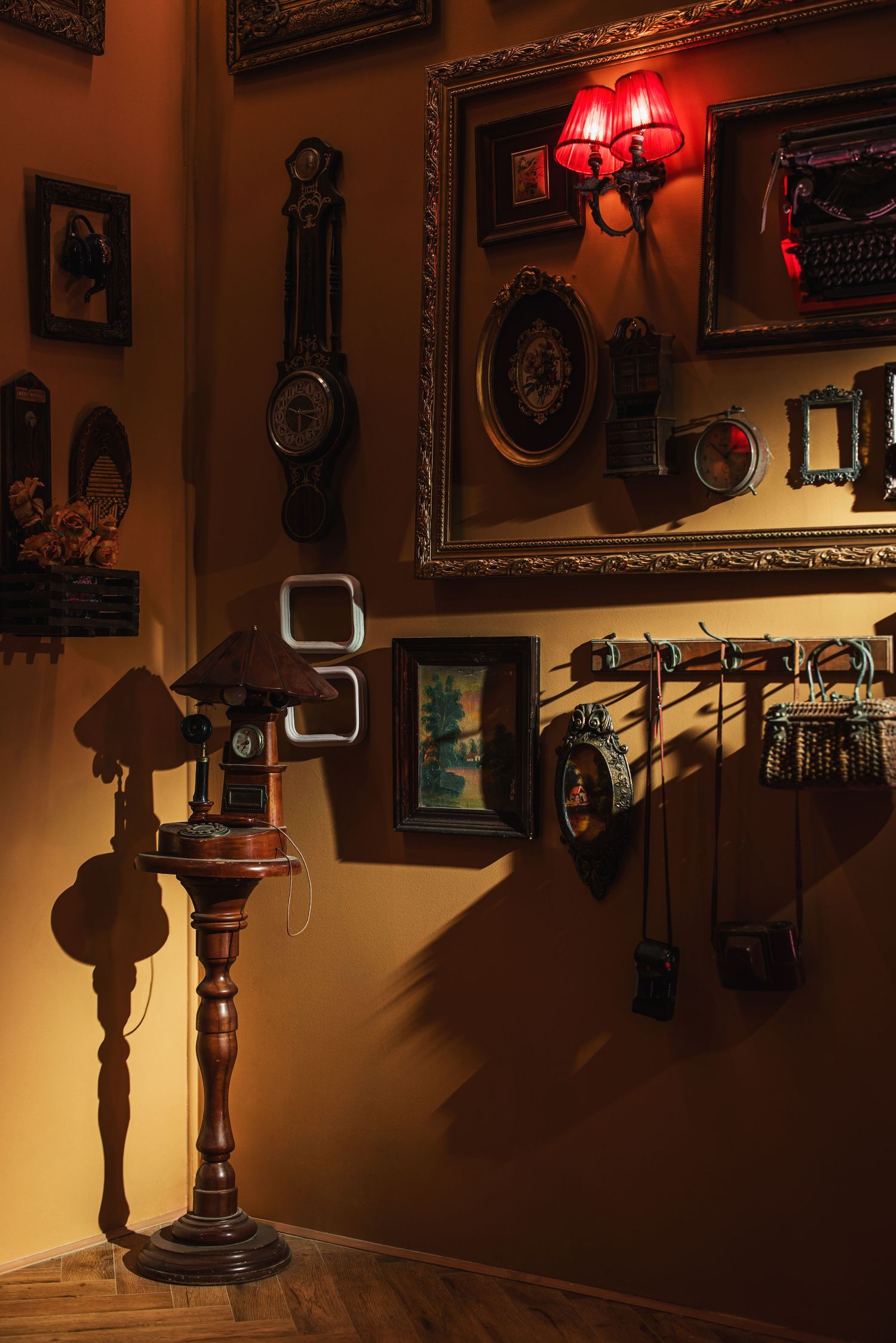 Antique wall display with vintage clocks, framed pictures, hanging bags, and red wall sconce lighting.