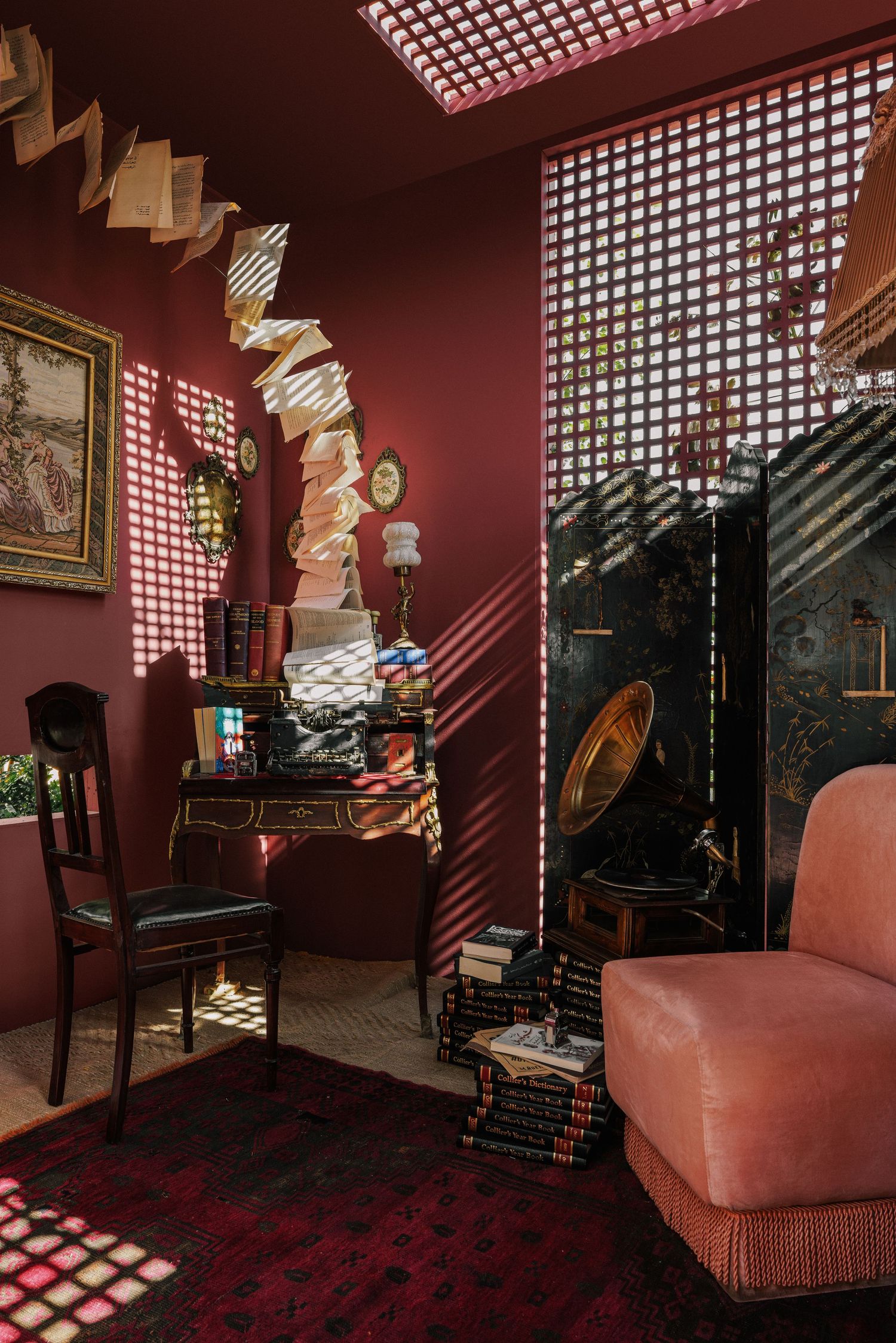 Vintage study room with deep red walls, antique desk, gramophone, stacked books, and floating pages.