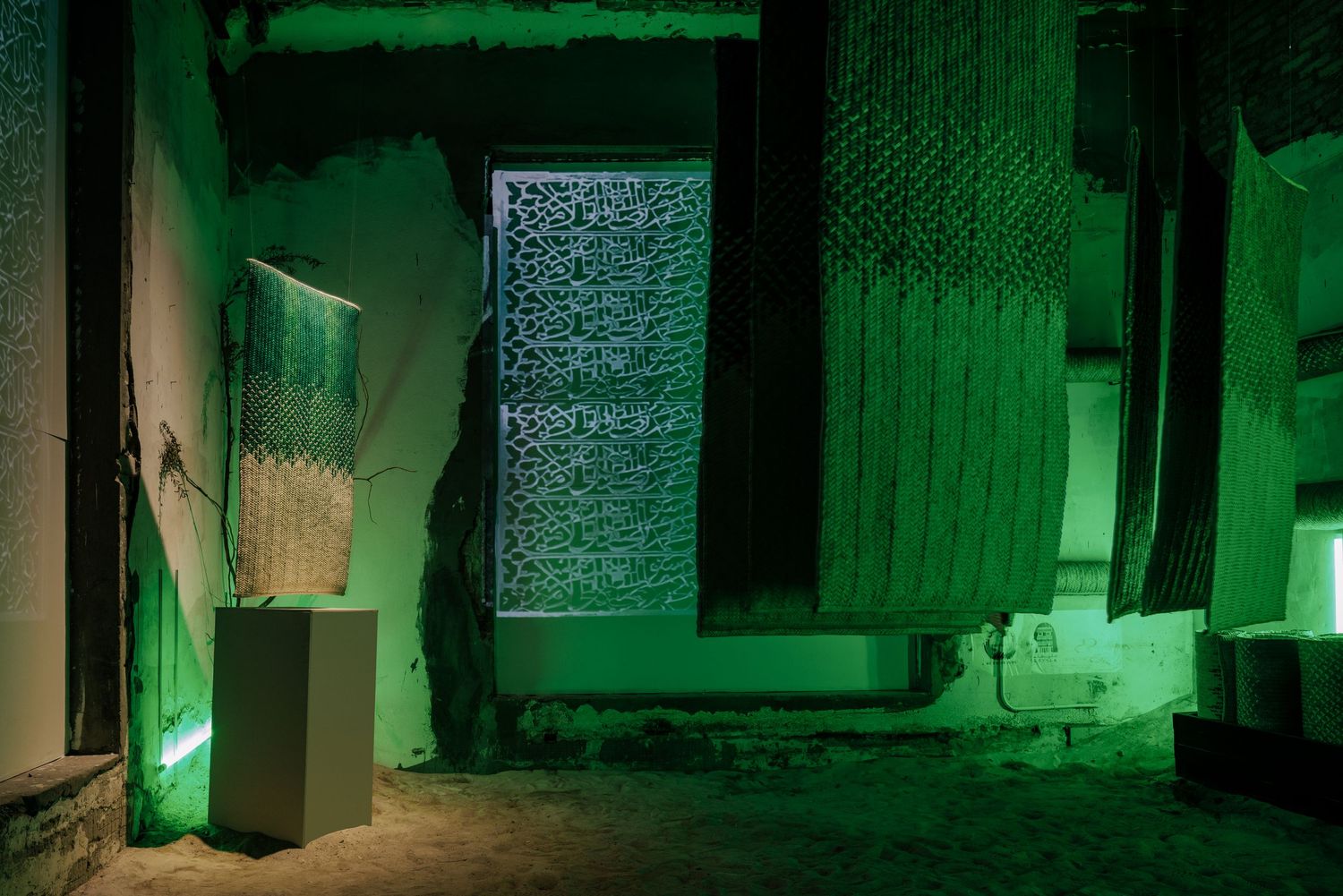 Green-lit art installation with translucent textile panels in a dimly lit abandoned interior space.