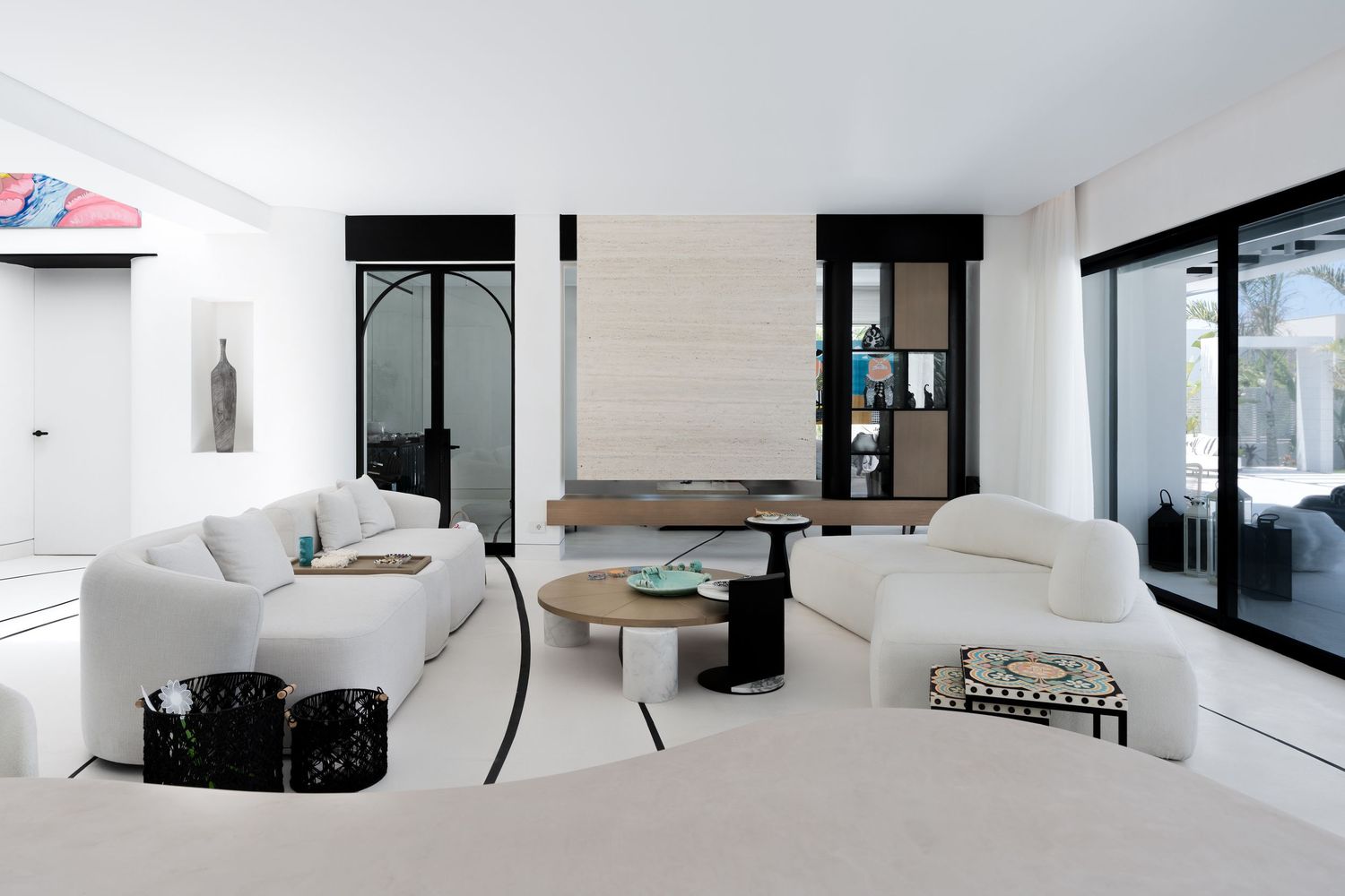 Sophisticated white living room with curved sofas, round table, fireplace, and black accent details.
