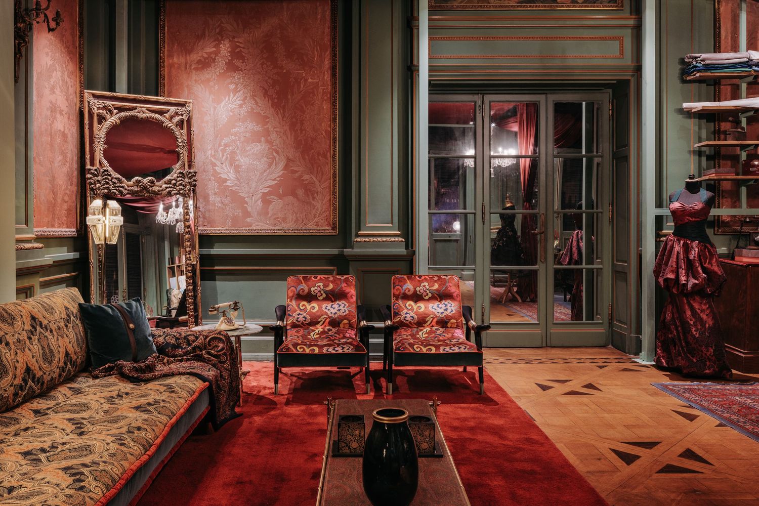 Luxurious vintage sitting room with red carpet, ornate mirror, patterned sofa, and classic armchairs.