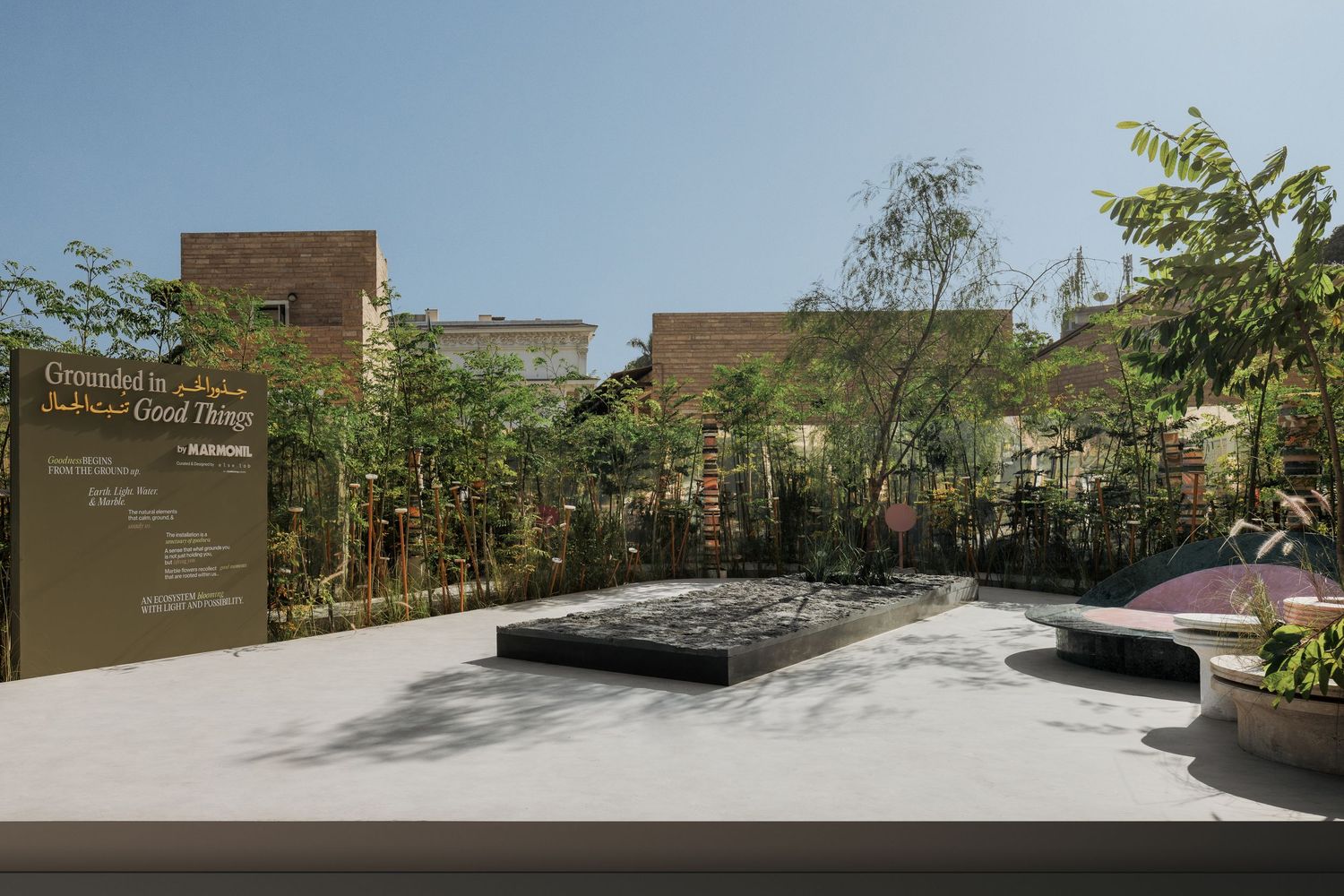 Minimalist outdoor garden installation with water feature and tropical plants under blue sky.