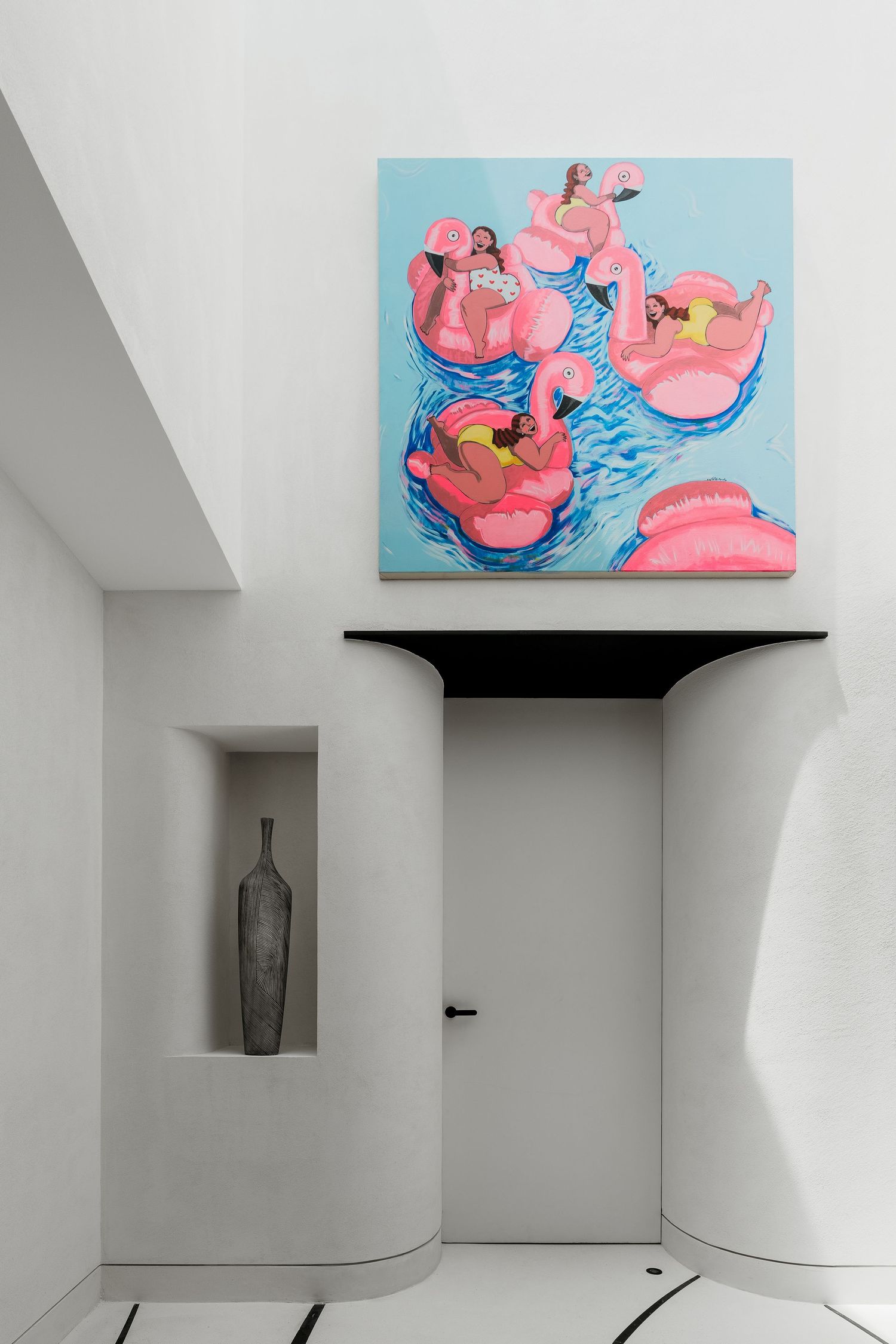 Minimalist white hallway featuring a vibrant painting of people on pink flamingo floats above a curved black shelf.