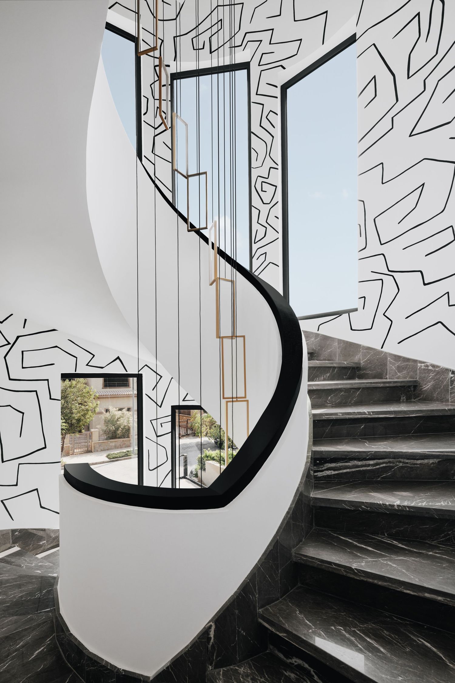 Elegant curved marble staircase with gold rod railing and bold black geometric line art walls.