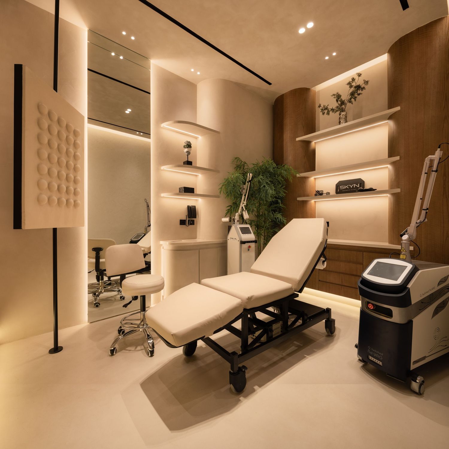 Elegant medical spa treatment room with white beds, built-in shelving, warm lighting, and laser equipment.