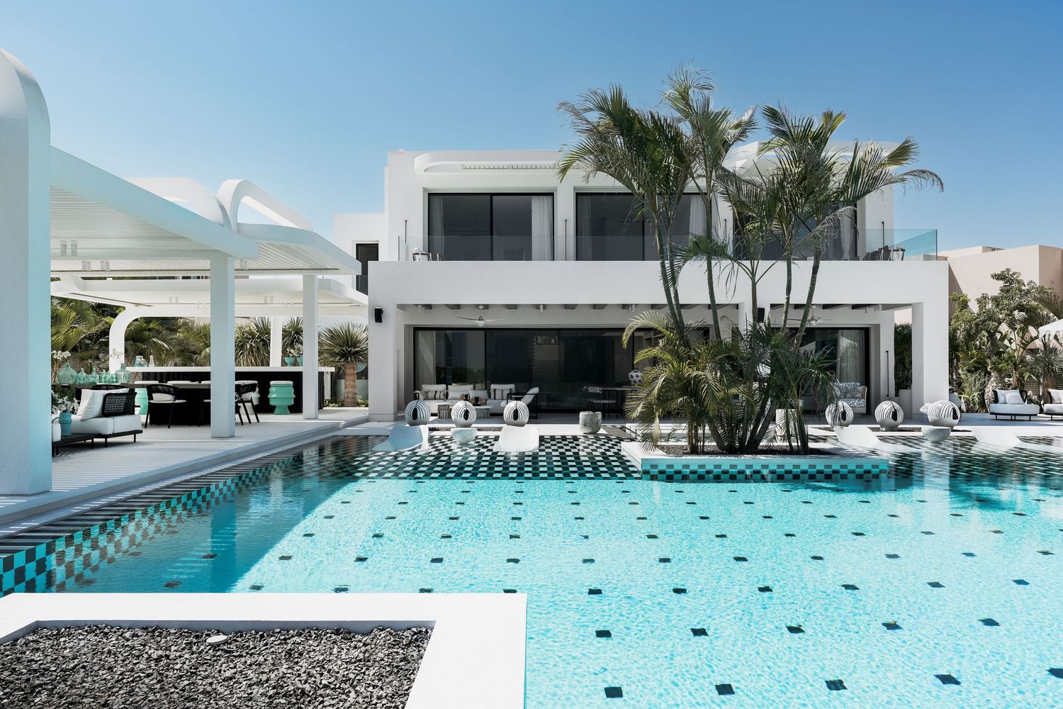 Luxury white modern villa with a stunning geometric pool featuring black and white tile accents and lush palm trees.