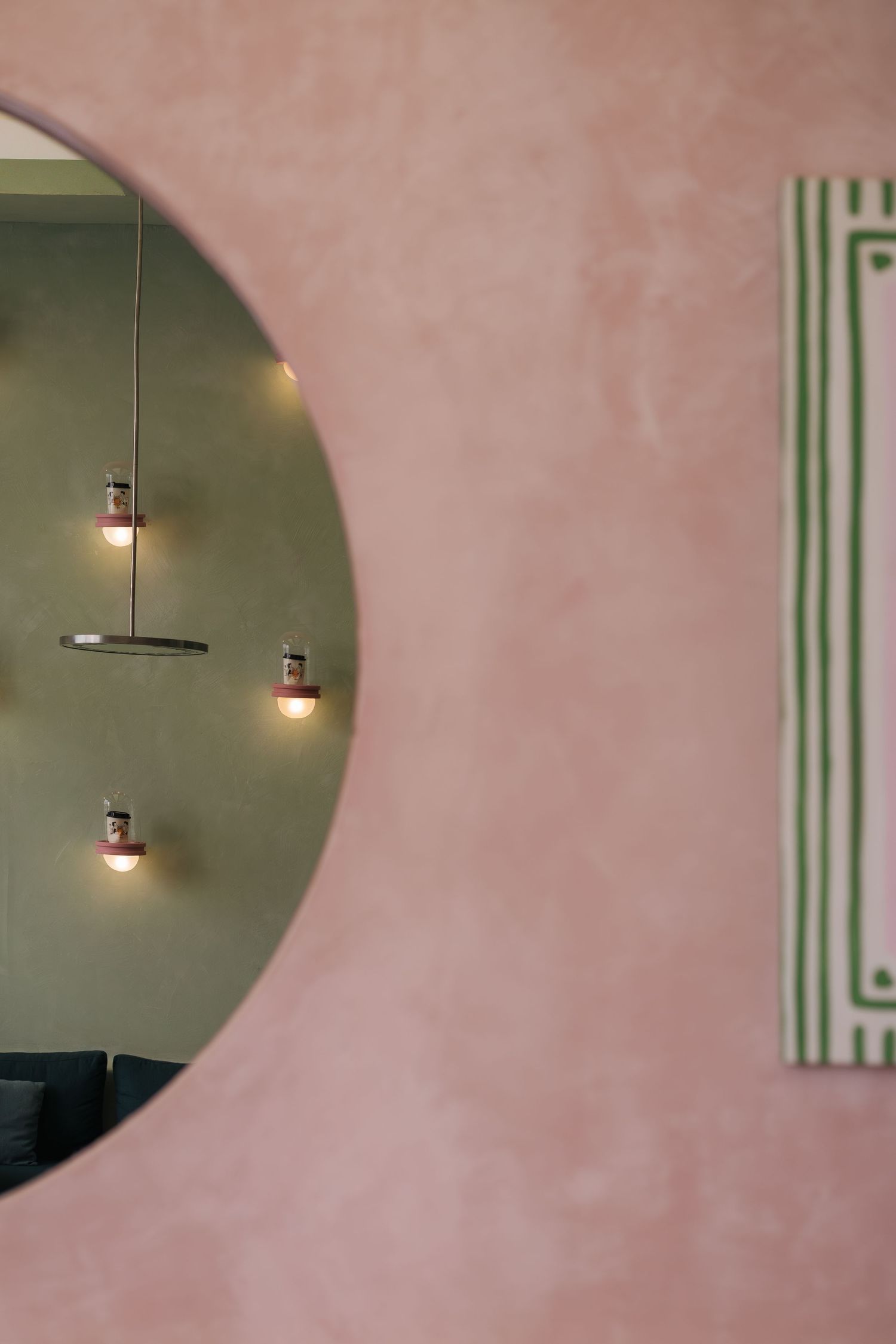 Pink textured wall with circular cutout revealing pendant lights and green striped artwork beside it.