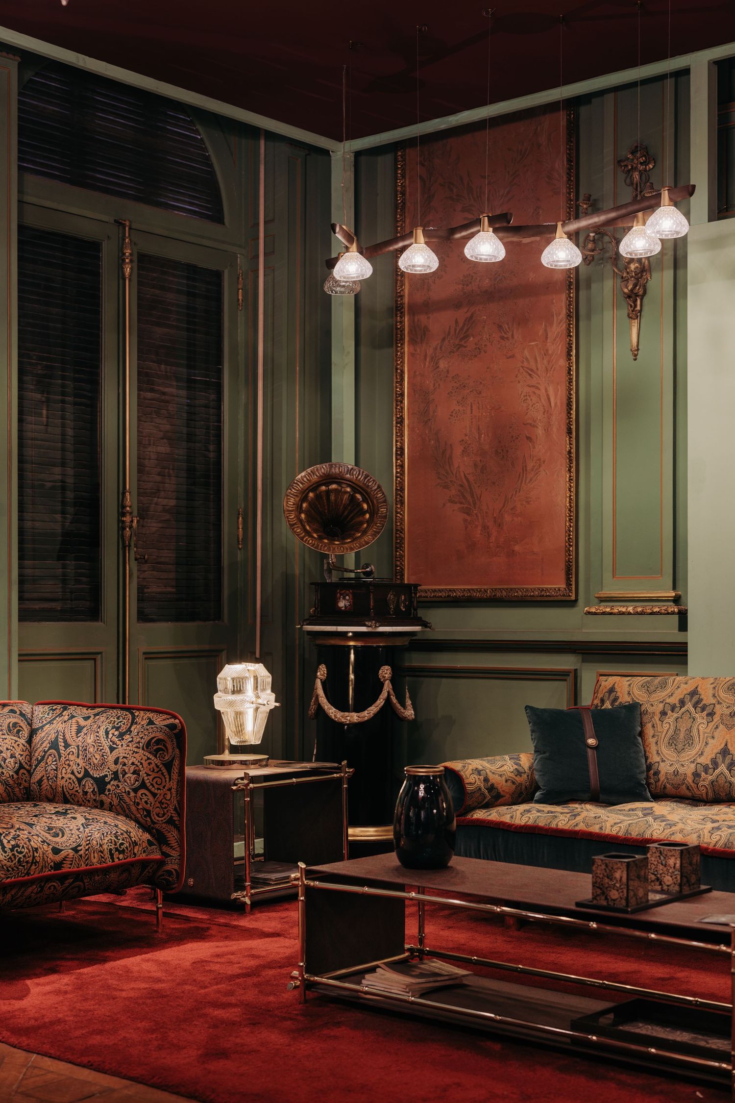 Elegant vintage living room with paisley sofas, red carpet, chandelier, and copper wall art.