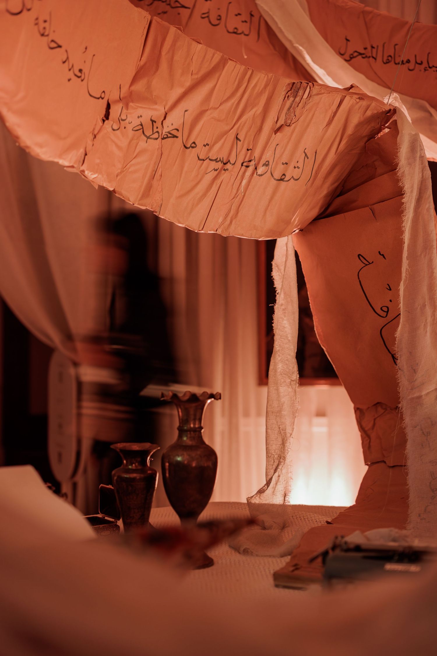 Flowing peach fabric canopy with Arabic calligraphy script draped over table with ceramic vases below.